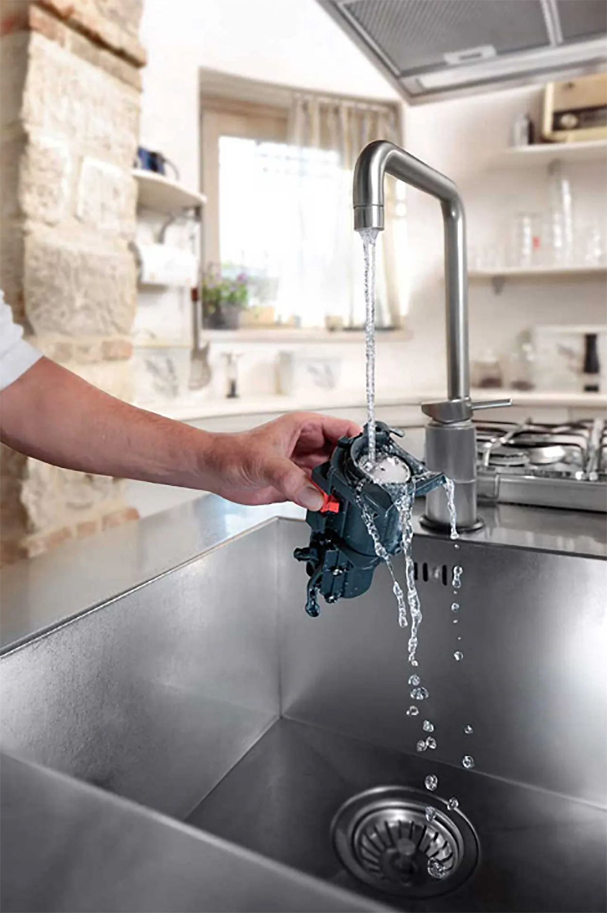 Eine Hand spült ein Geschirrteil unter einem Wasserhahn in einem Waschbecken ab.