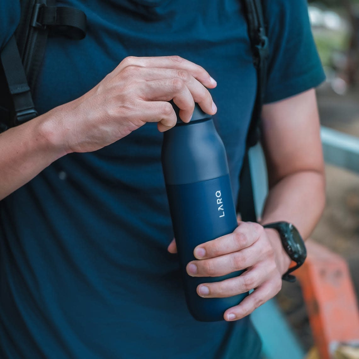 Person hält eine dunkelblaue LARQ-Wasserflasche vor einem verschwommenen Hintergrund.
