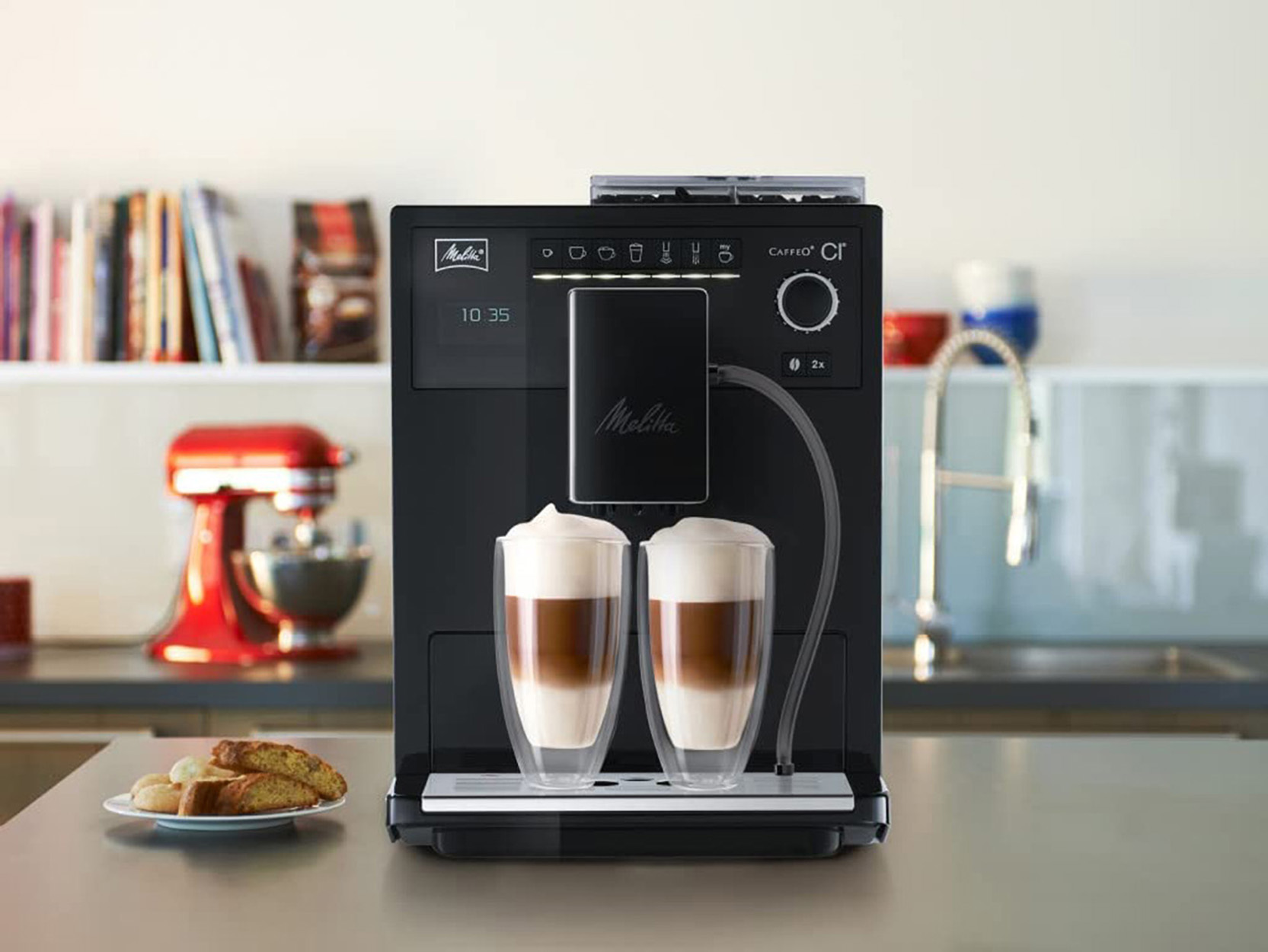 Schwarze Melitta Caffeo CI Kaffeemaschine. Zwei Gläser mit Latte und Biscotti auf der Theke.