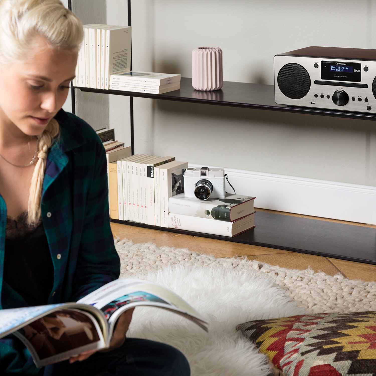 Frau liest Zeitschrift, Kamera und Bücher auf Regal. Radio ist auf dem Regal sichtbar.