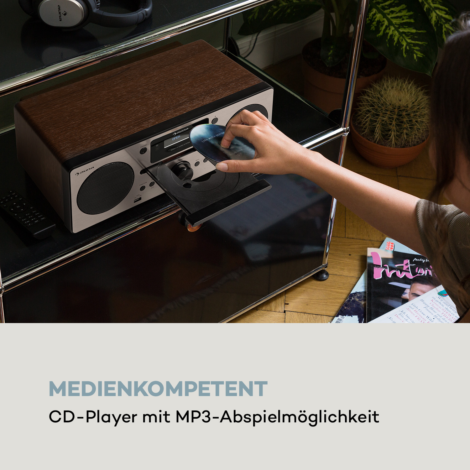 Eine Hand legt eine CD in einen CD-Player ein. Andere Objekte sind in der Szene.