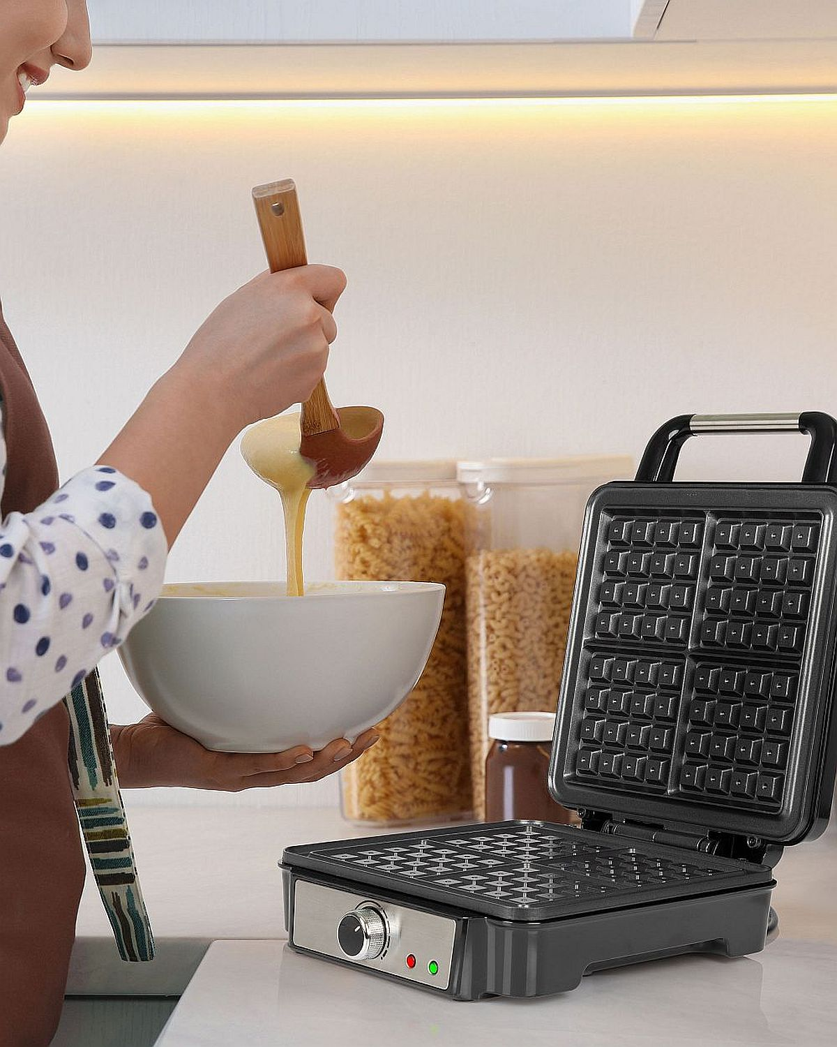 Eine Person gießt Teig aus einer Schüssel in einen Waffeleisen.