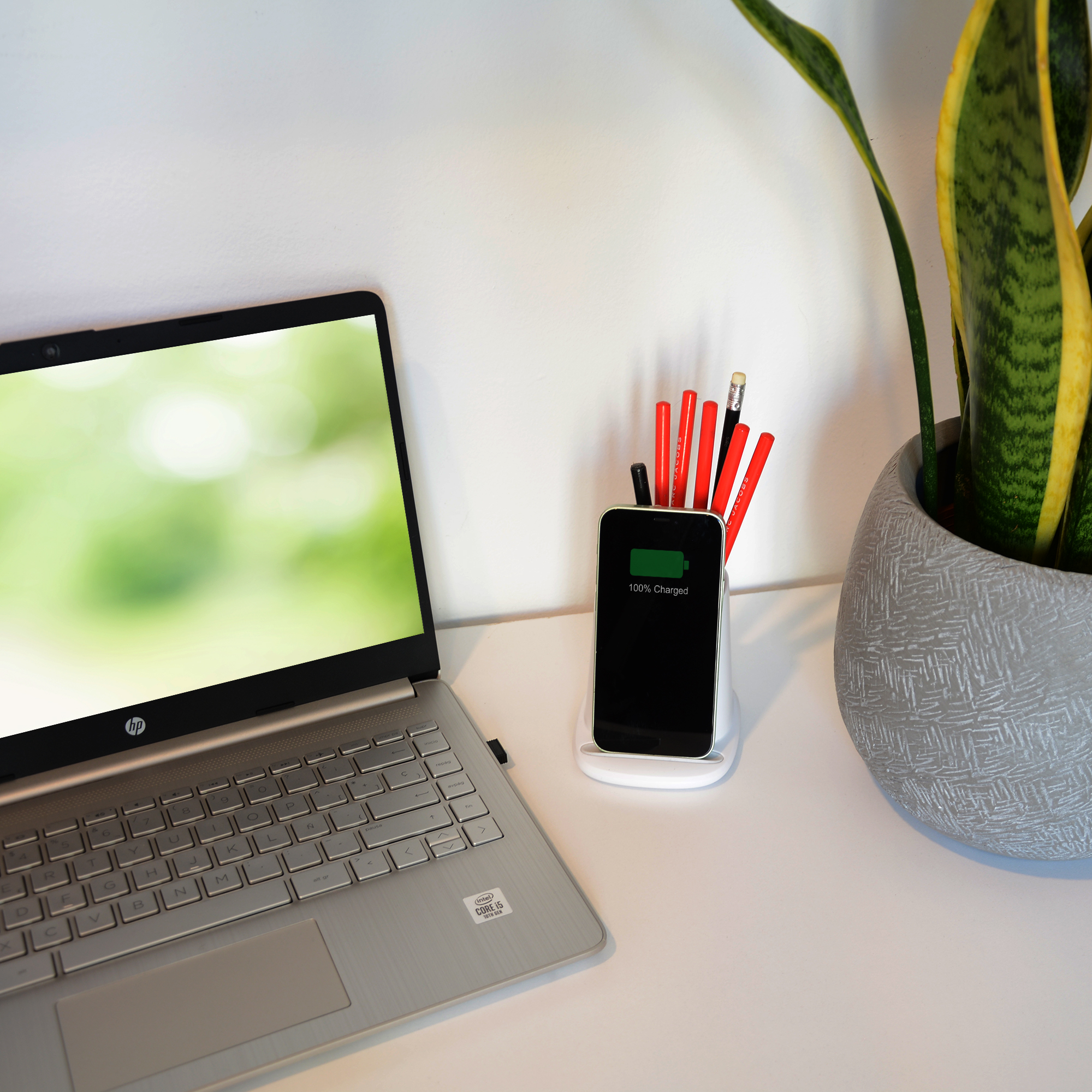 Una laptop junto a un teléfono cargando en un soporte sobre un escritorio blanco.
