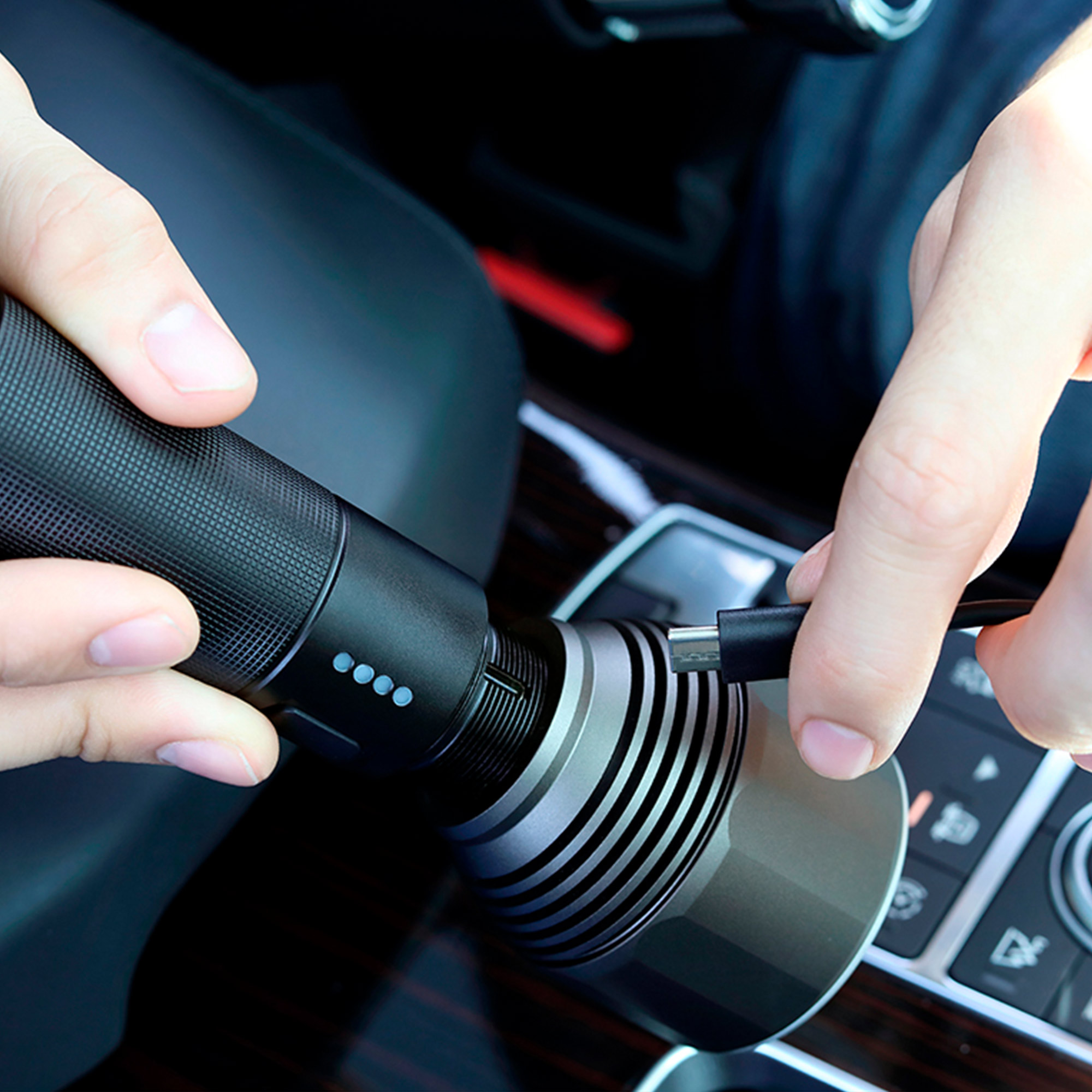 Manos conectan cable USB a linterna negra en un coche.