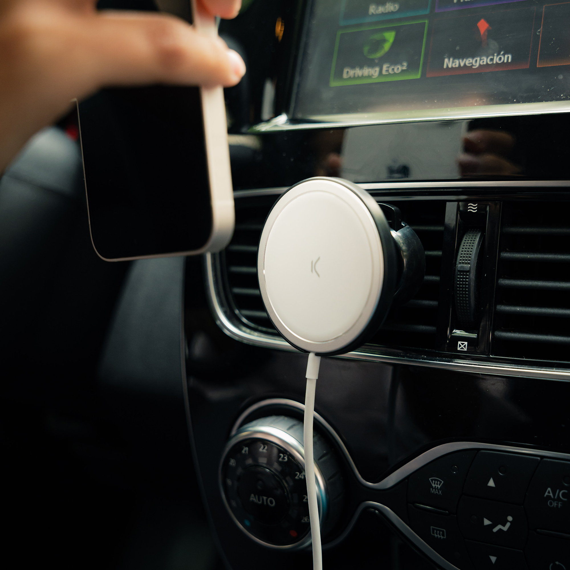 Mano sosteniendo un teléfono blanco cerca de una rejilla de ventilación del coche. Soporte magnético blanco.