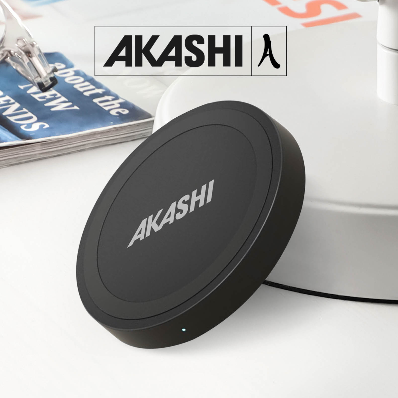 Cargador inalámbrico negro y redondo de la marca Akashi sobre una superficie blanca. El logotipo de Akashi está en el cargador.