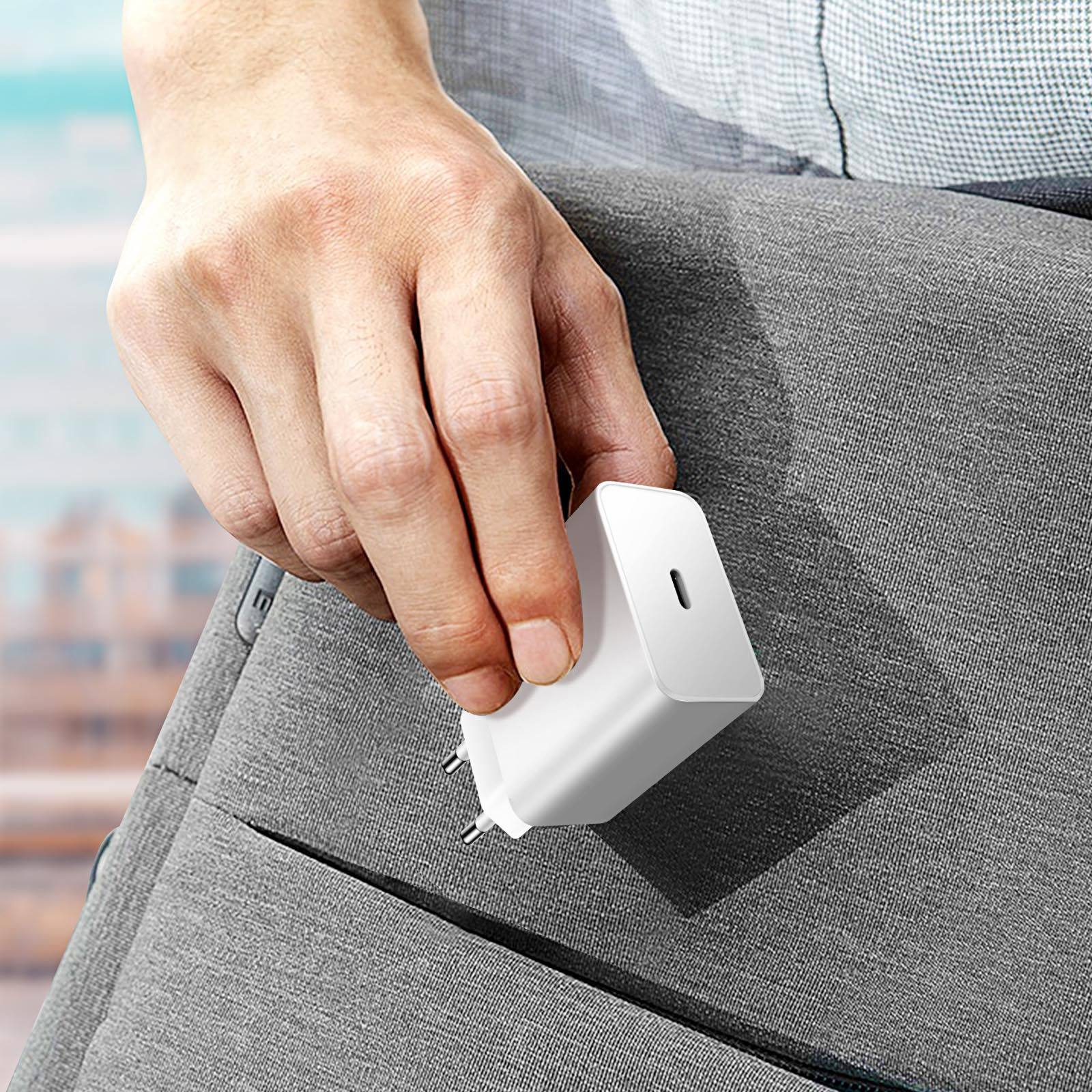 Un cargador blanco con puerto USB-C se sostiene cerca de una bolsa gris. El cargador tiene un enchufe de dos clavijas.