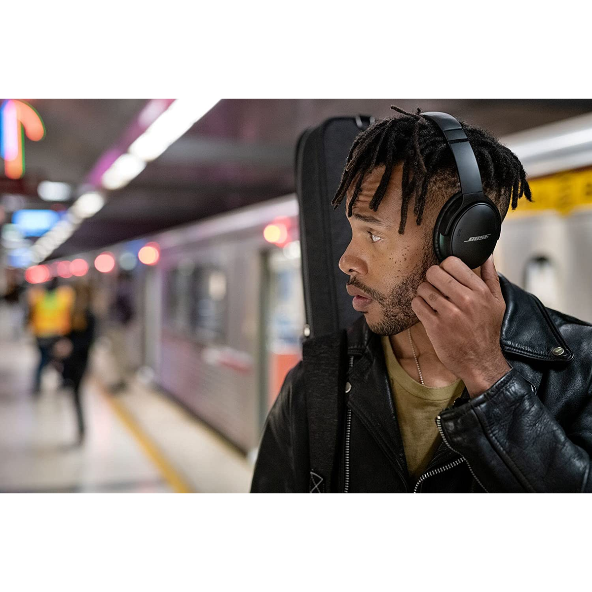 Mann in U-Bahn mit Kopfhörern und Gitarrenkoffer. U-Bahn im Hintergrund.
