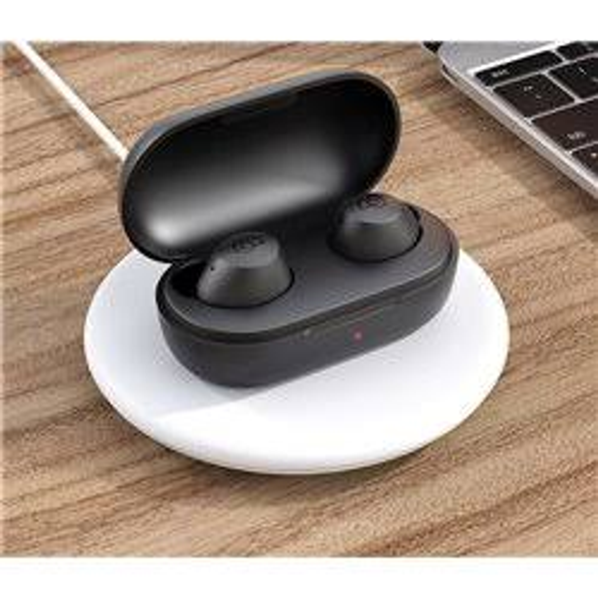 Auricolari wireless neri in una custodia di ricarica su un tappetino di ricarica bianco. Un laptop sullo sfondo.