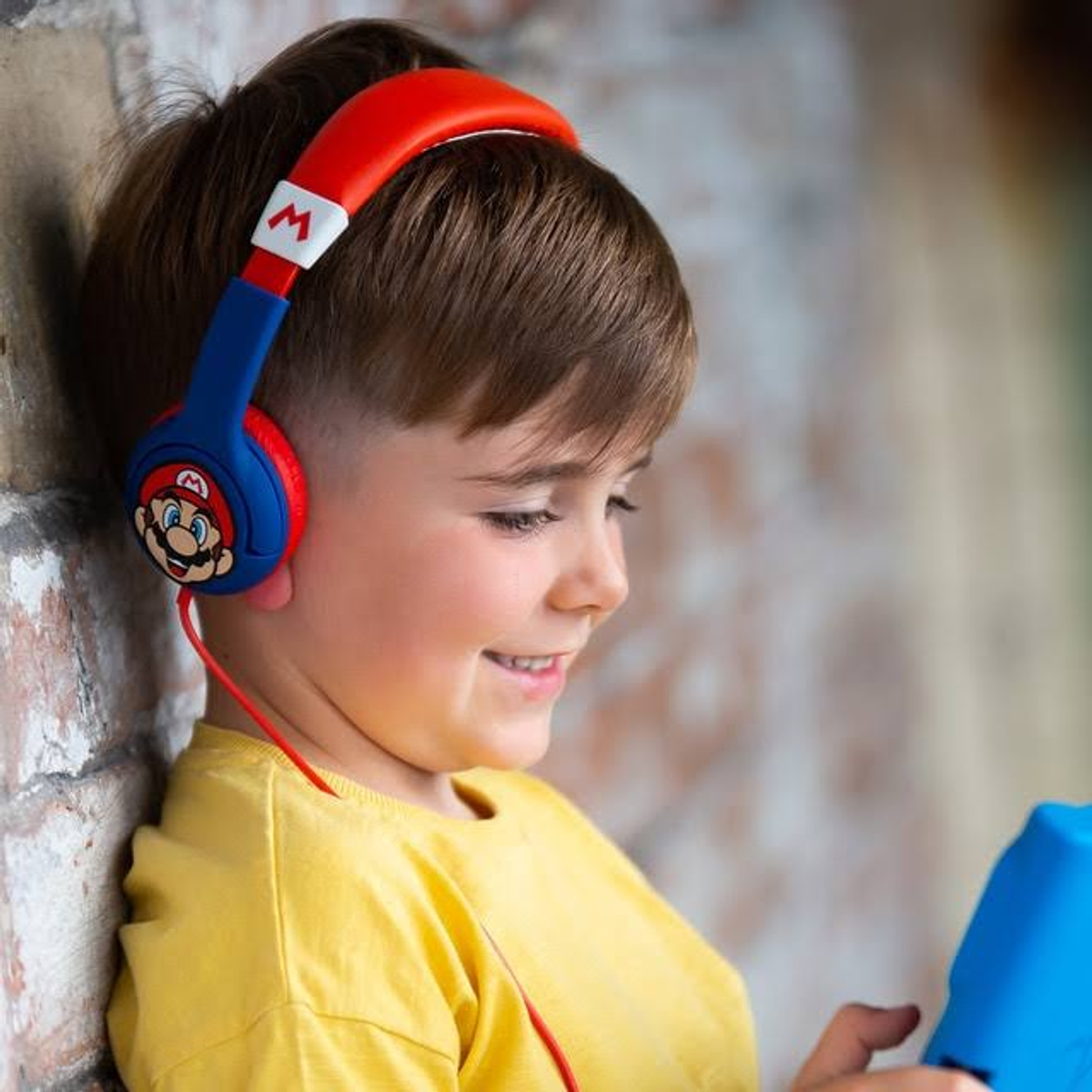 Młody chłopiec w słuchawkach Mario uśmiecha się, patrząc na tablet.