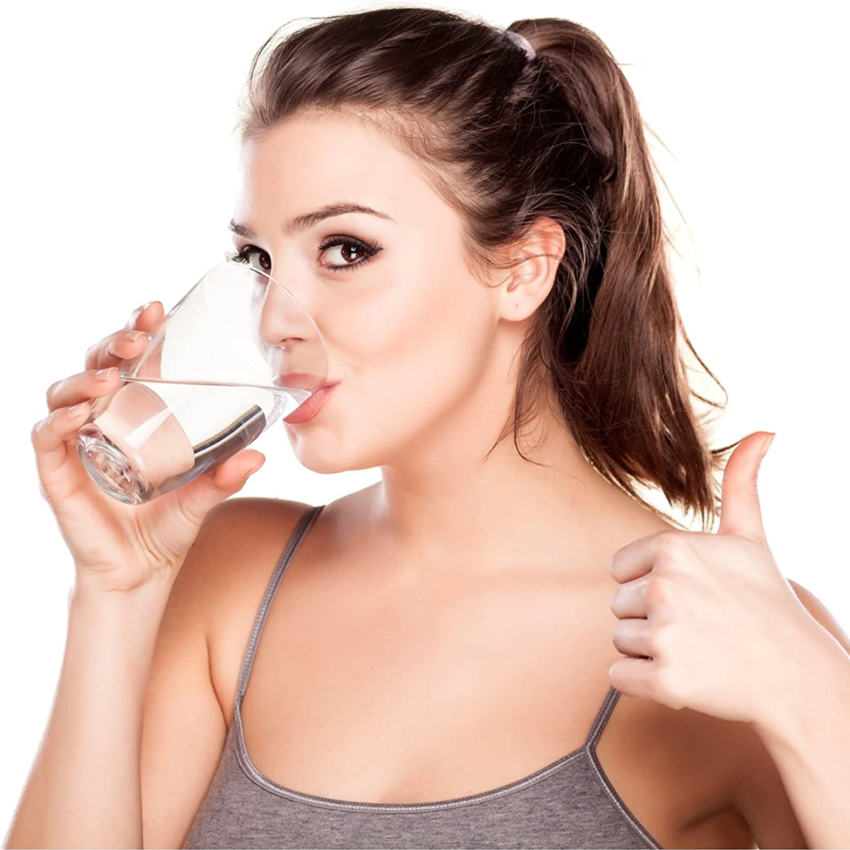 Donna che beve acqua, pollice in su. Bicchiere trasparente, sfondo bianco.