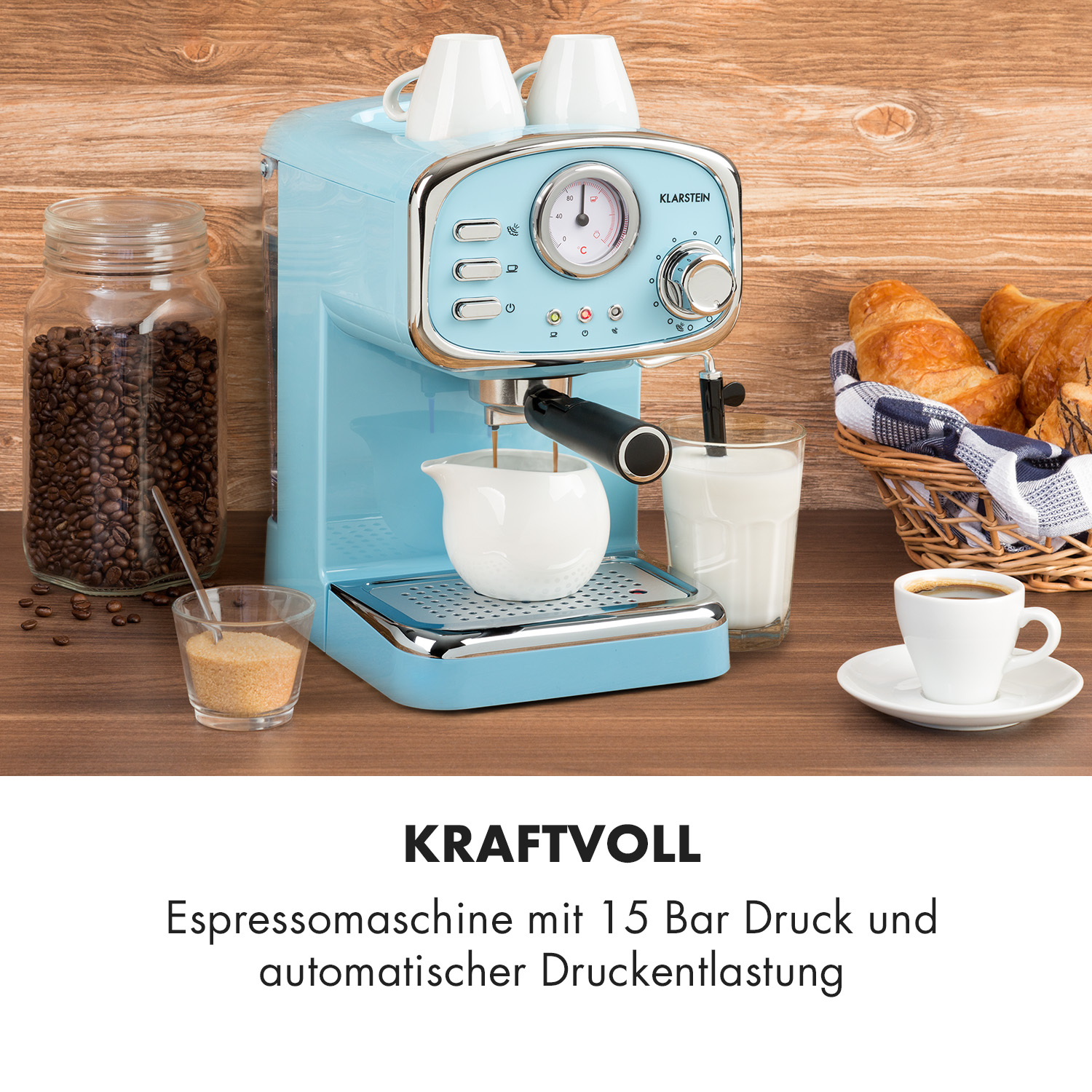 Eine hellblaue Espressomaschine im Retro-Stil. Auf dem Tisch befinden sich Kaffeebohnen, Tassen und Croissants.