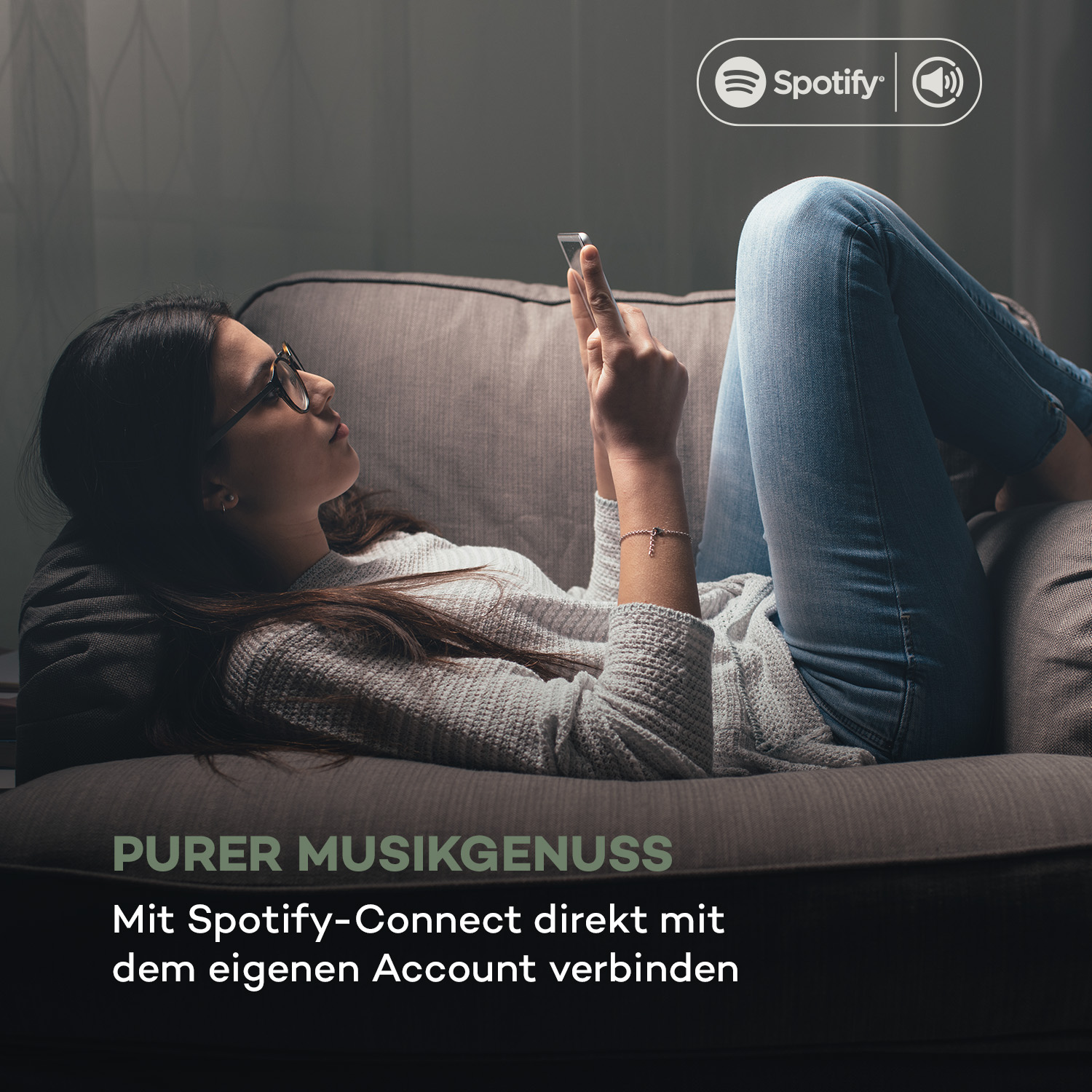 Eine Person liegt auf einem Sofa und benutzt ein Telefon mit Spotify-Logo.
