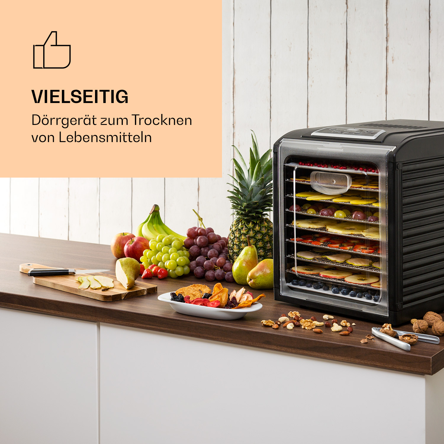 Schwarzer Dörrautomat mit getrockneten Lebensmitteln, Obst und Nüssen auf Holz.