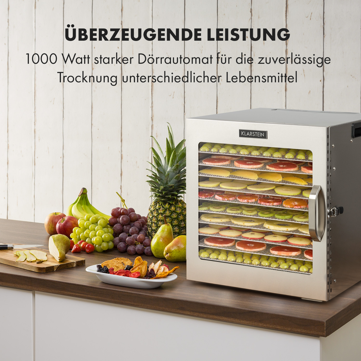 Edelstahl-Lebensmitteltrockner mit verschiedenen Früchten und Gemüse auf Regalen. Text: „Überzeugende Leistung“.