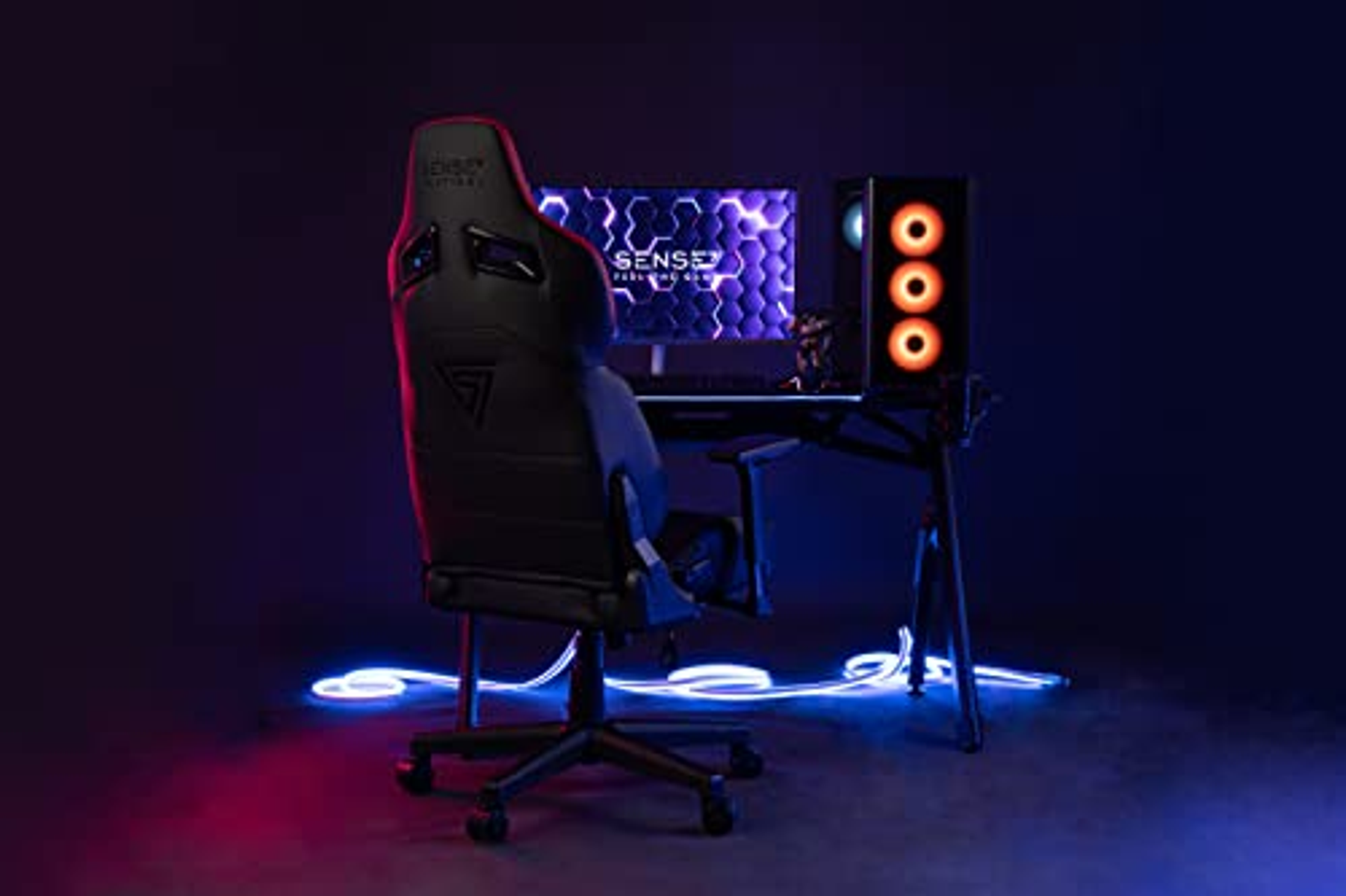 Een zwarte gamingopstelling met een stoel op de voorgrond. Het bureau heeft een monitor en pc-componenten met lichten.