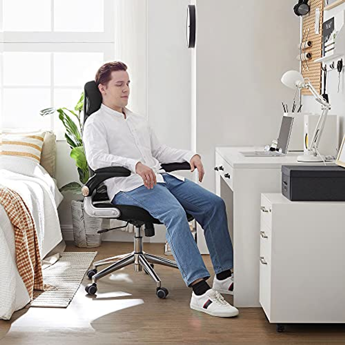 Un uomo seduto su una sedia nera a una scrivania. Indossa una camicia bianca e jeans. C'è un laptop.