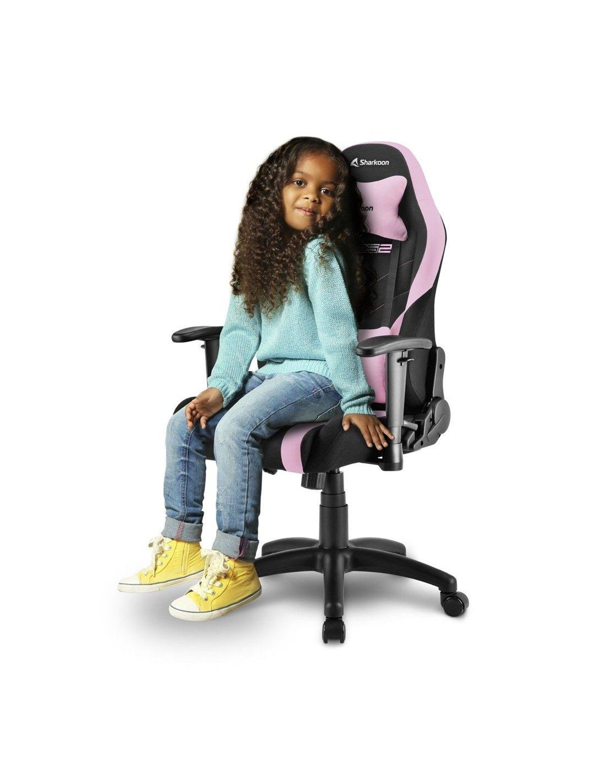 Niña sentada en una silla gaming rosa y negra, sonriendo. Fondo blanco.