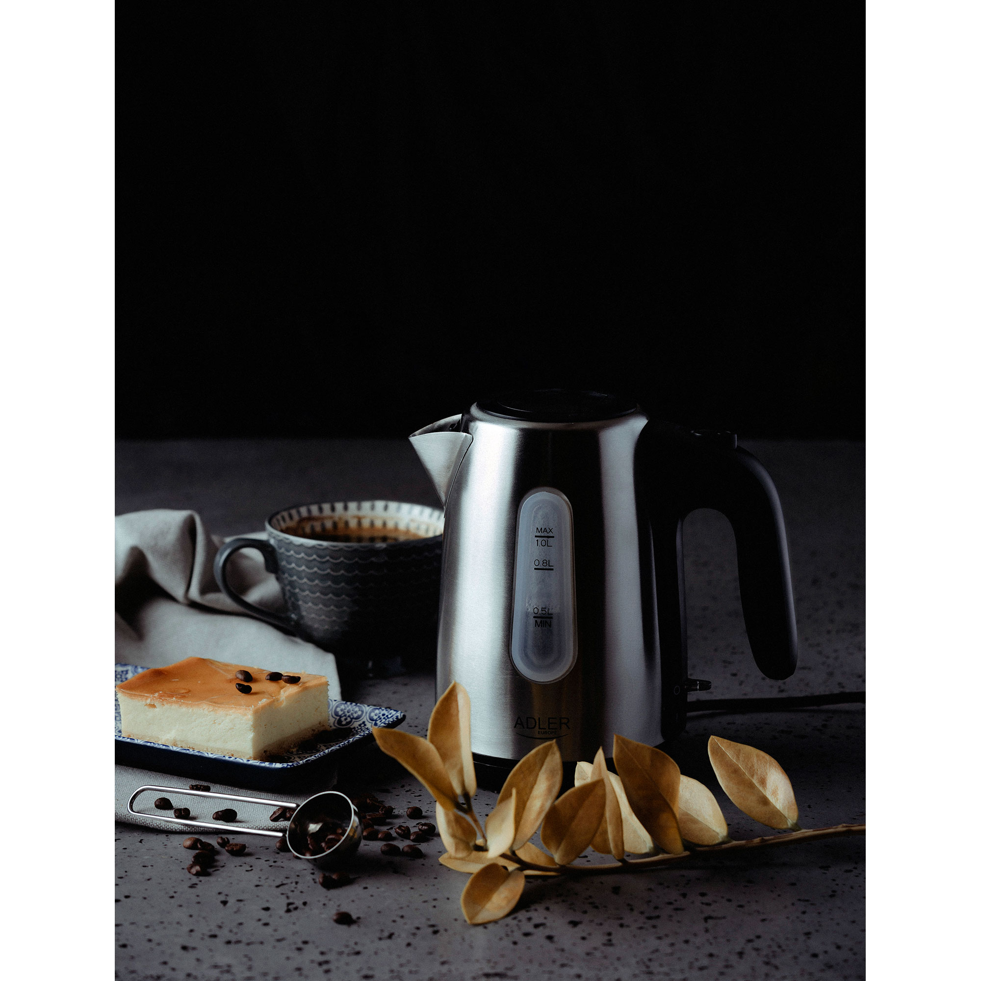 Bouilloire électrique à côté d'une tasse de café, gâteau, grains de café et feuilles.