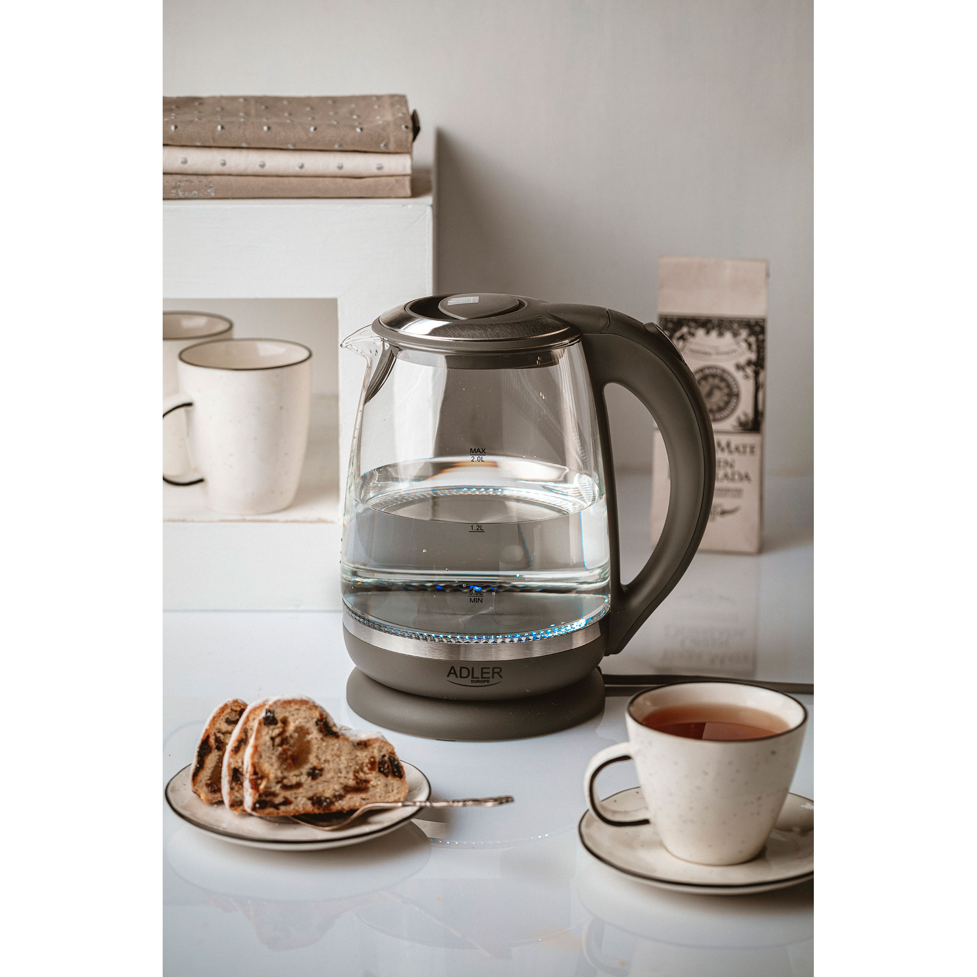 Bouilloire électrique en verre avec de l'eau, à côté d'une tasse de thé et gâteau.