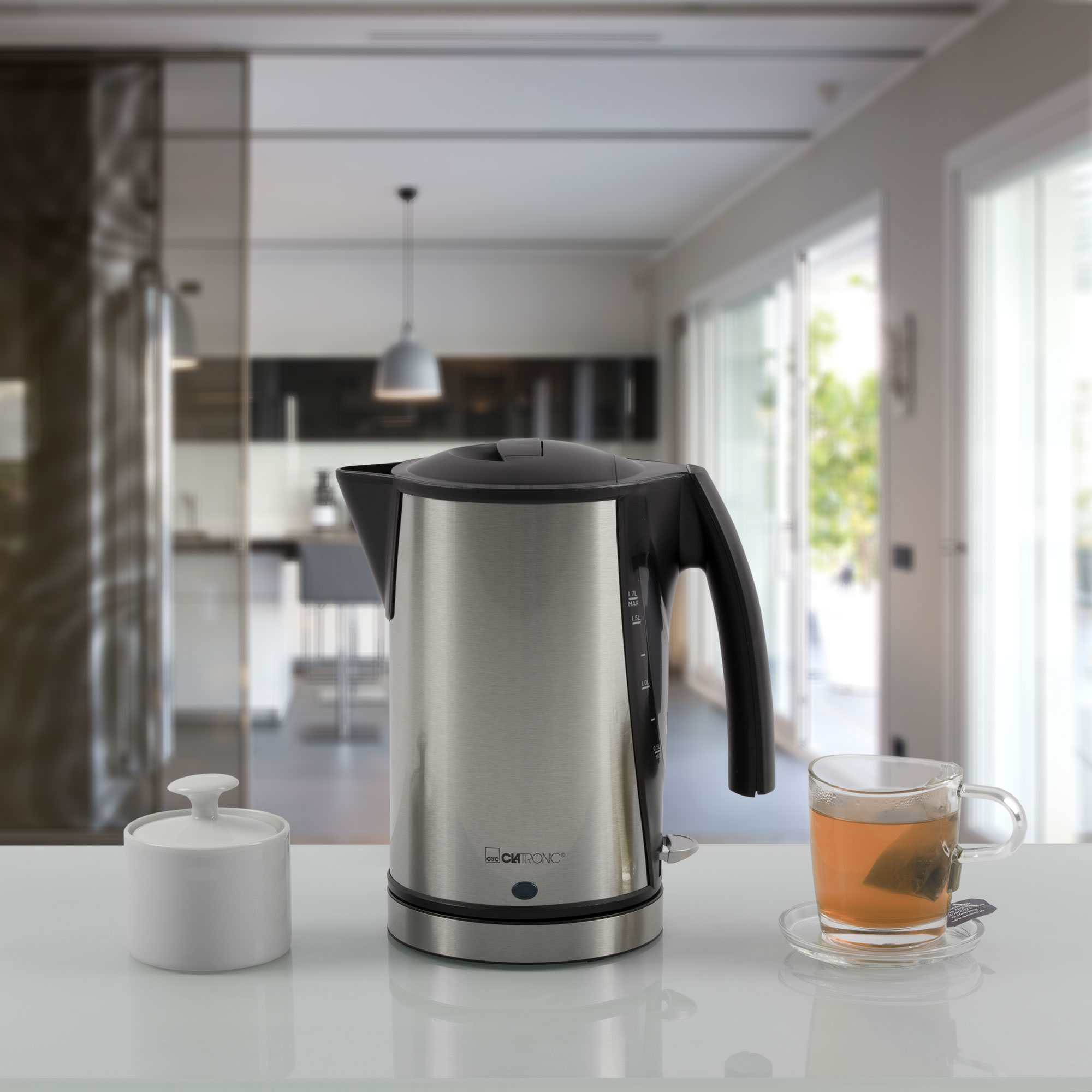 Hervidor eléctrico de acero inoxidable, azucarero y una taza de té. Superficie blanca.