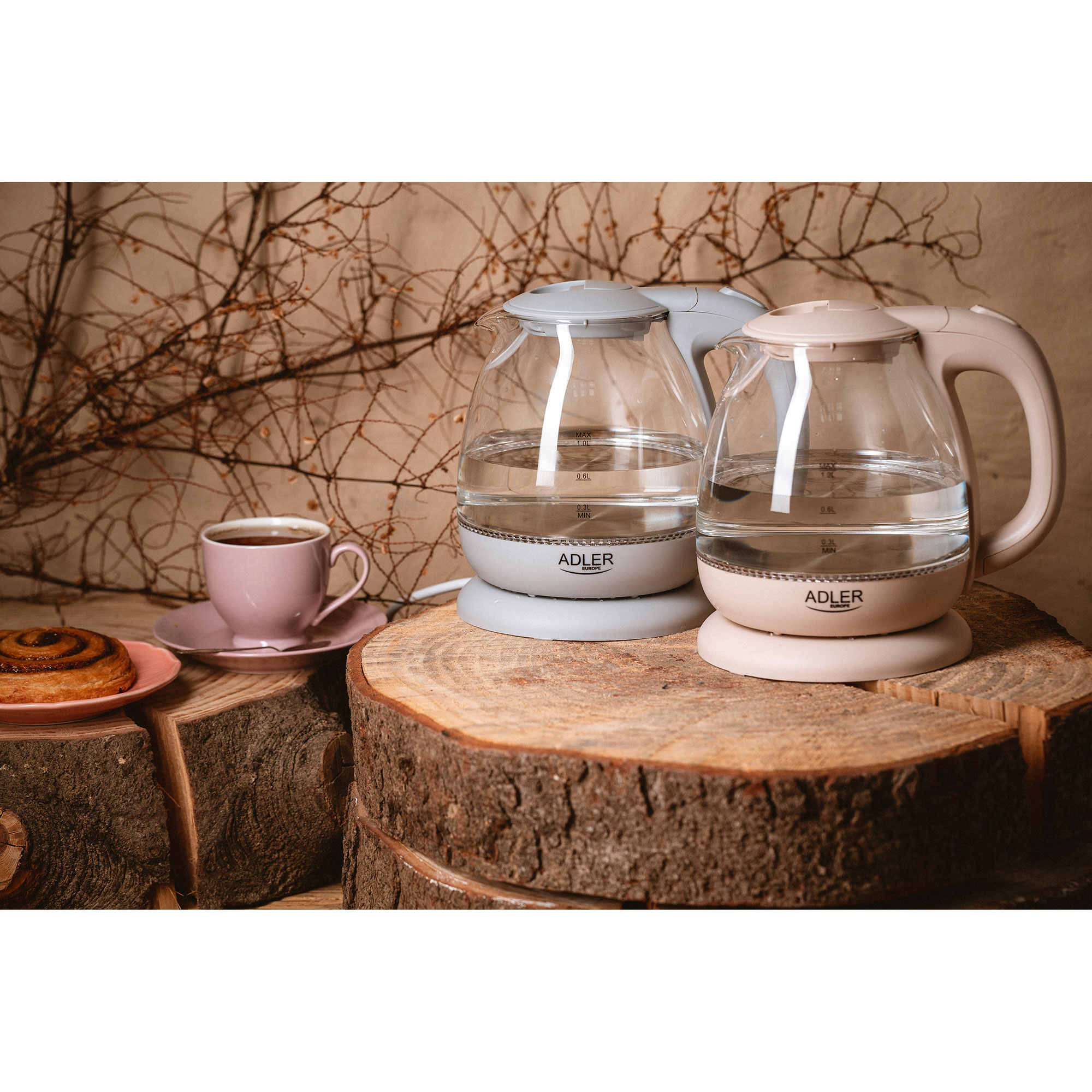 Dos hervidores de vidrio con agua sobre una superficie de madera, con una taza de café y pastelería.