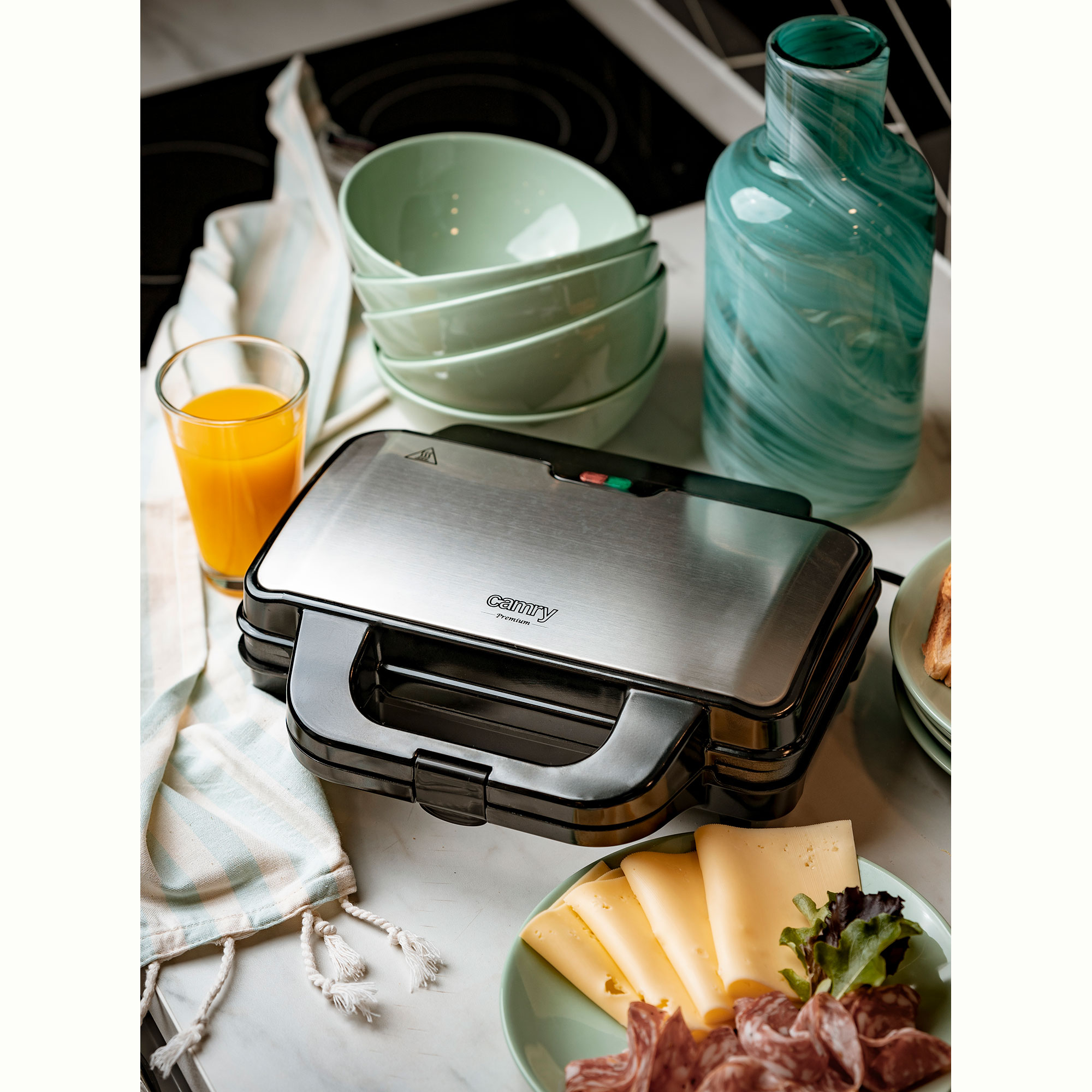 Toster do kanapek, miski z jedzeniem i szklanka soku pomarańczowego na marmurowym blacie.