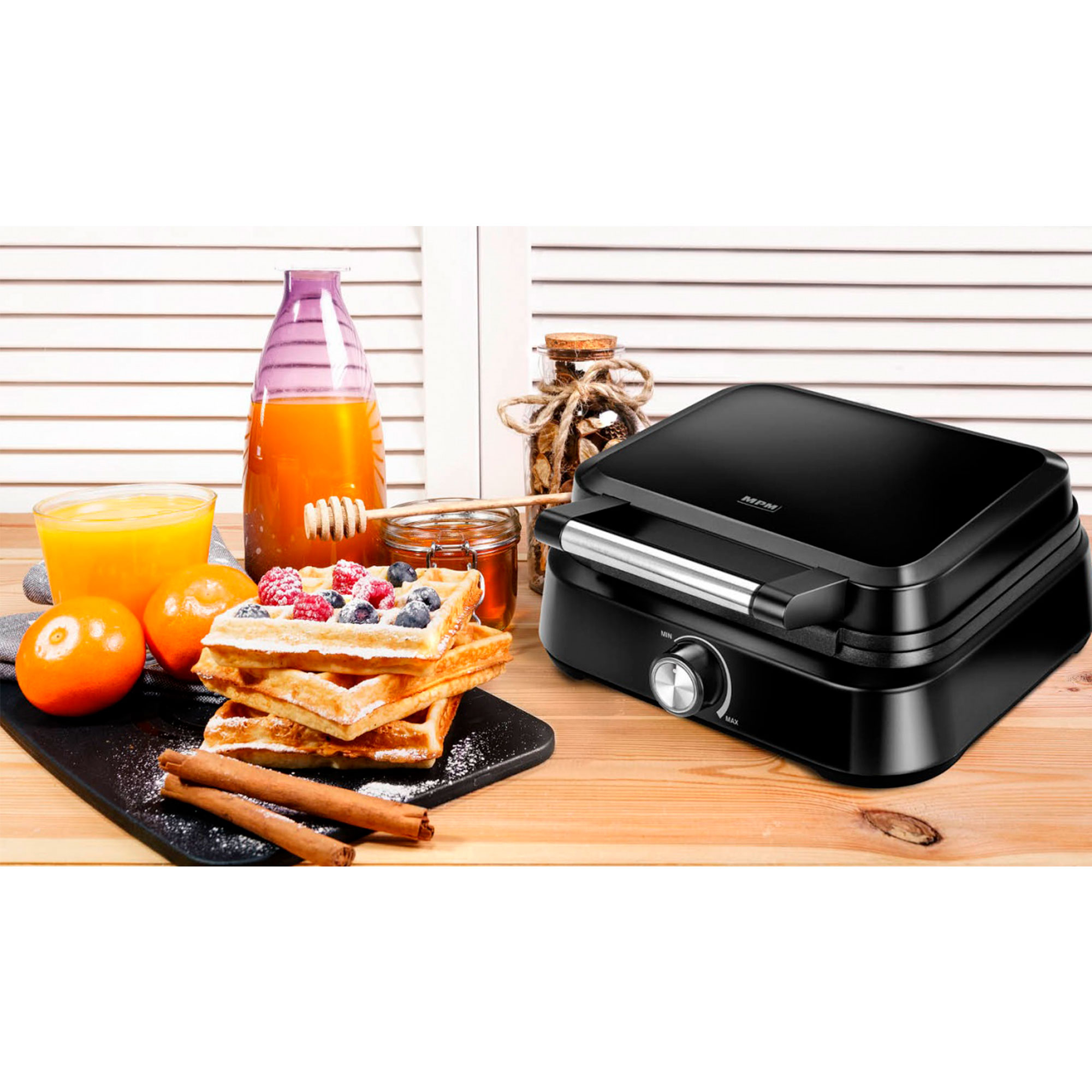 Czarny gofrownica z goframi, owocami i syropem. Na drewnianym stole, blisko okna.