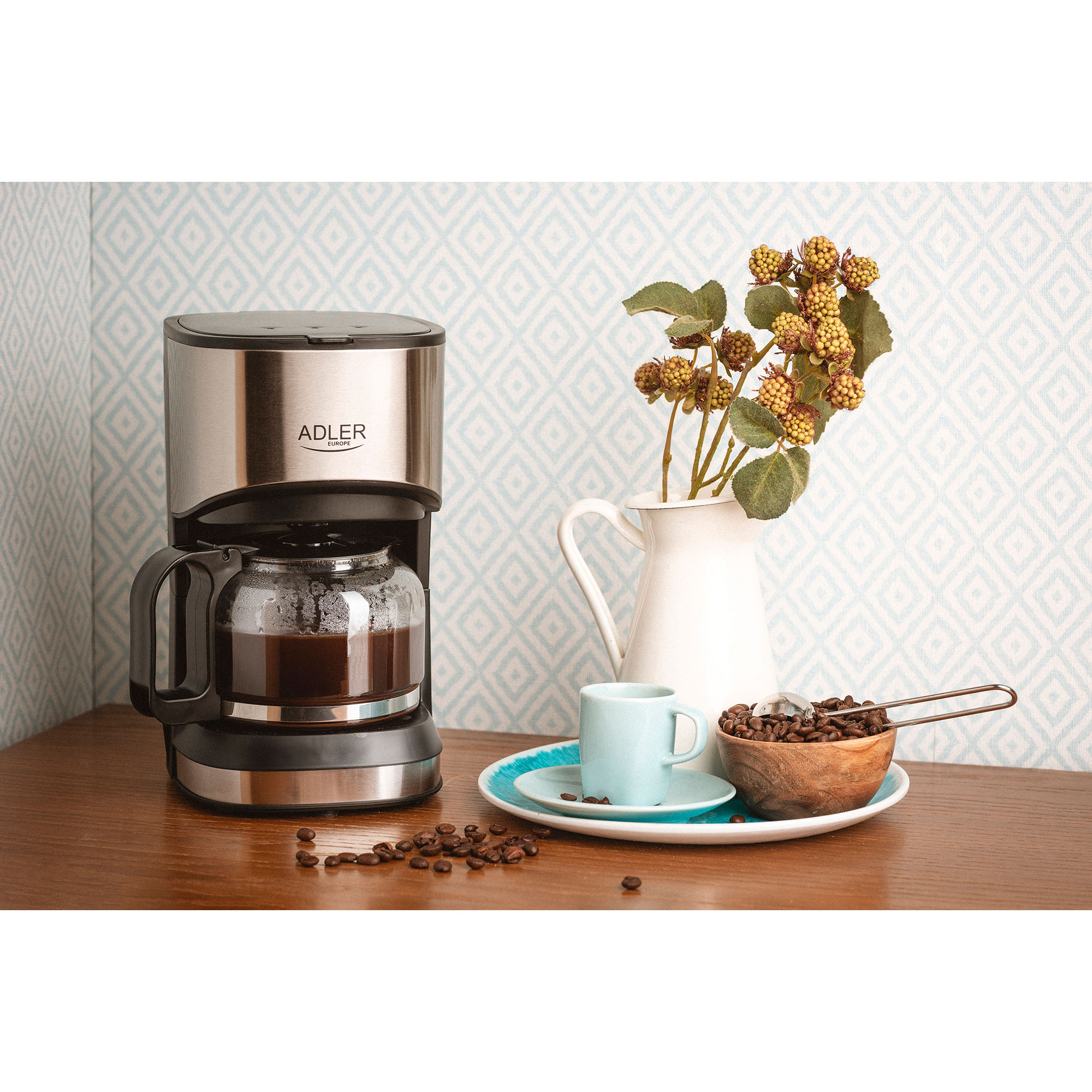 Ekspres do kawy z dzbankiem do kawy na drewnianym stole. Kwiaty w wazonie, ziarna kawy oraz filiżanka i spodek.