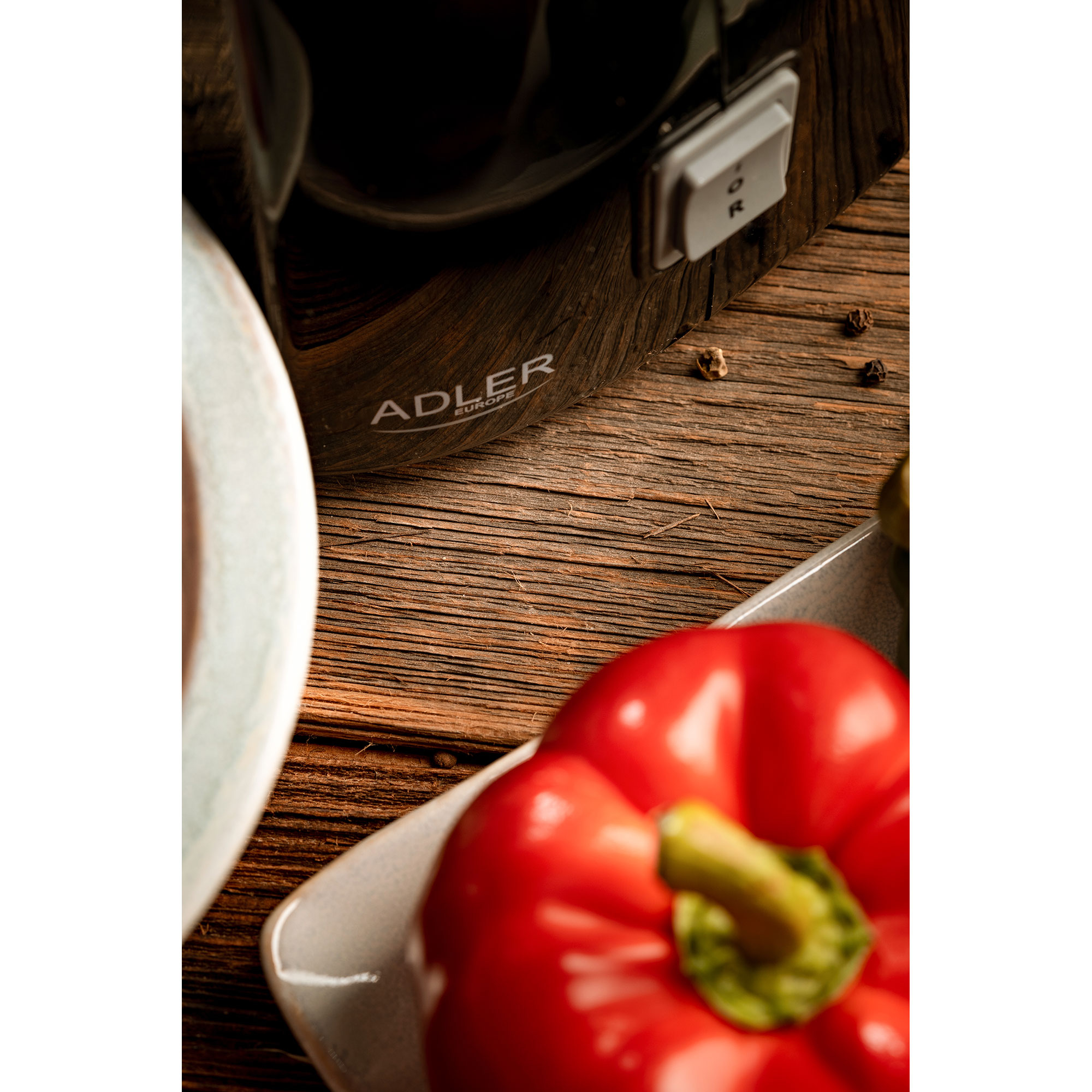 Primo piano di peperone rosso, piatto e elettrodomestico nero con il logo 'ADLER'.