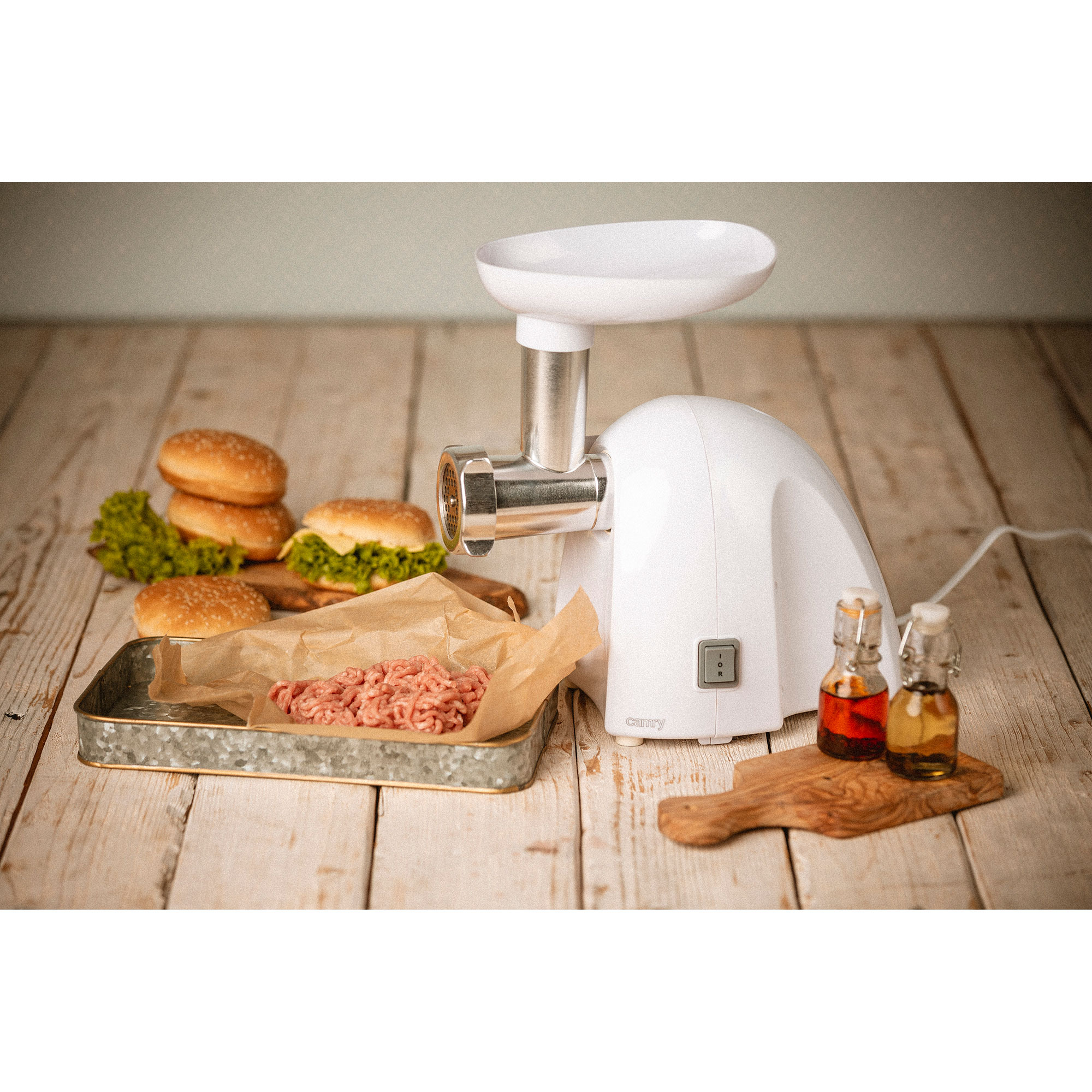 Biała maszynka do mięsa z mielonym mięsem i dodatkami do burgerów. Umieszczona na drewnianej powierzchni.