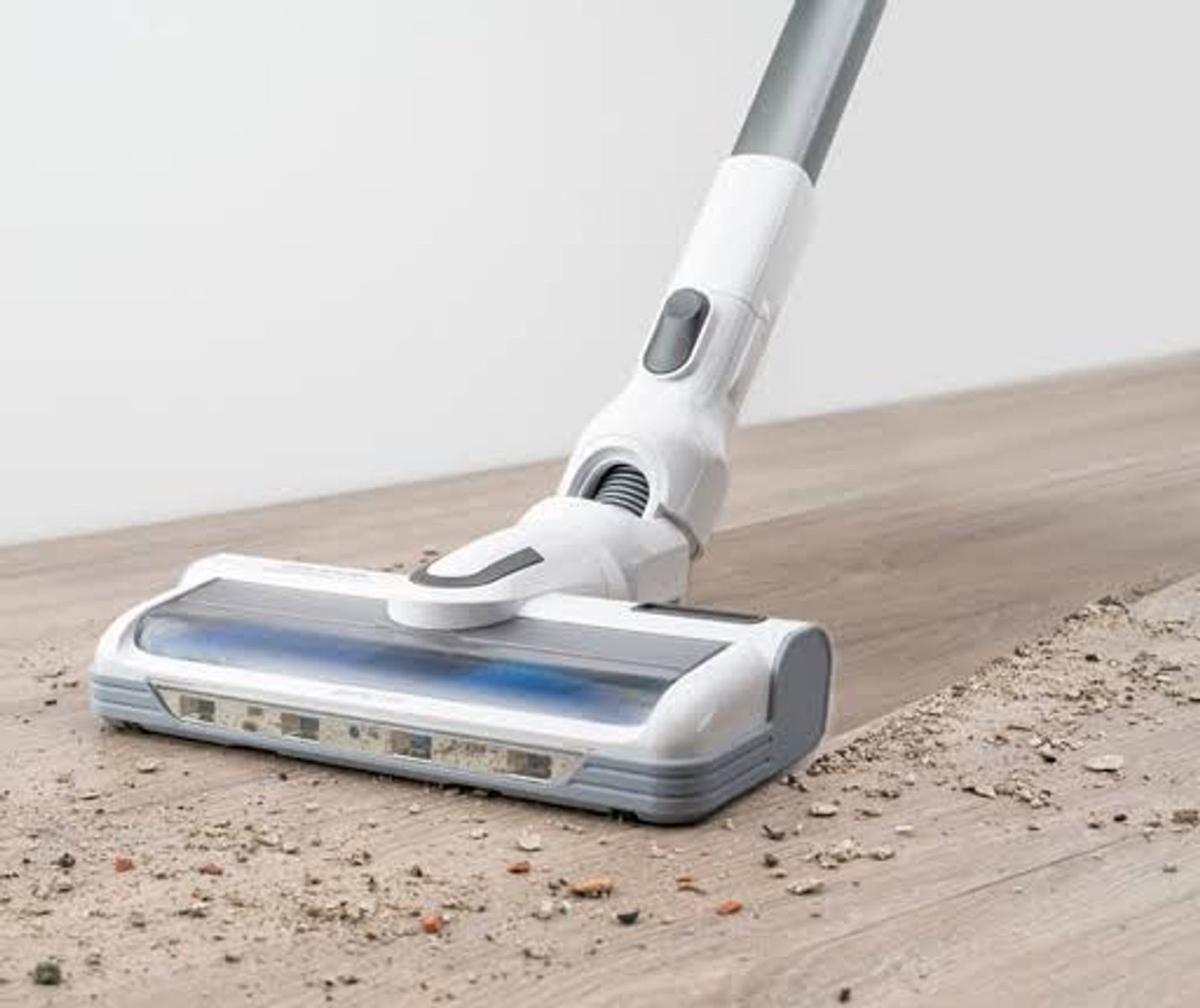 Una testina per aspirapolvere bianca e grigia che pulisce un pavimento in legno con sporco visibile.