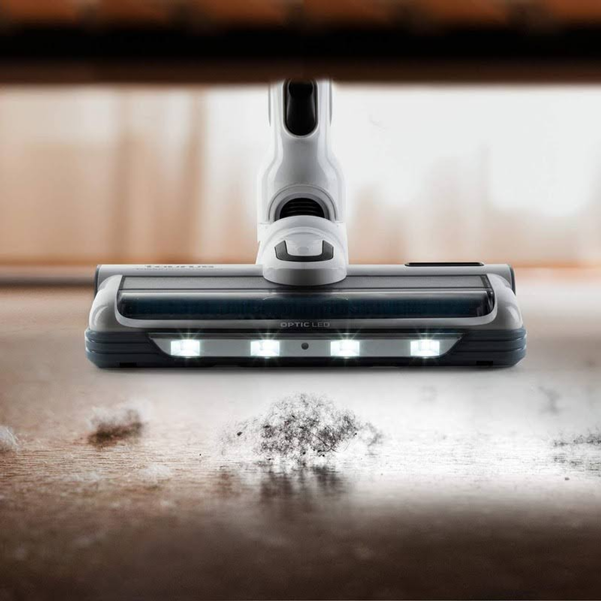Primo piano di una testina per aspirapolvere con luci e particelle di polvere sul pavimento.