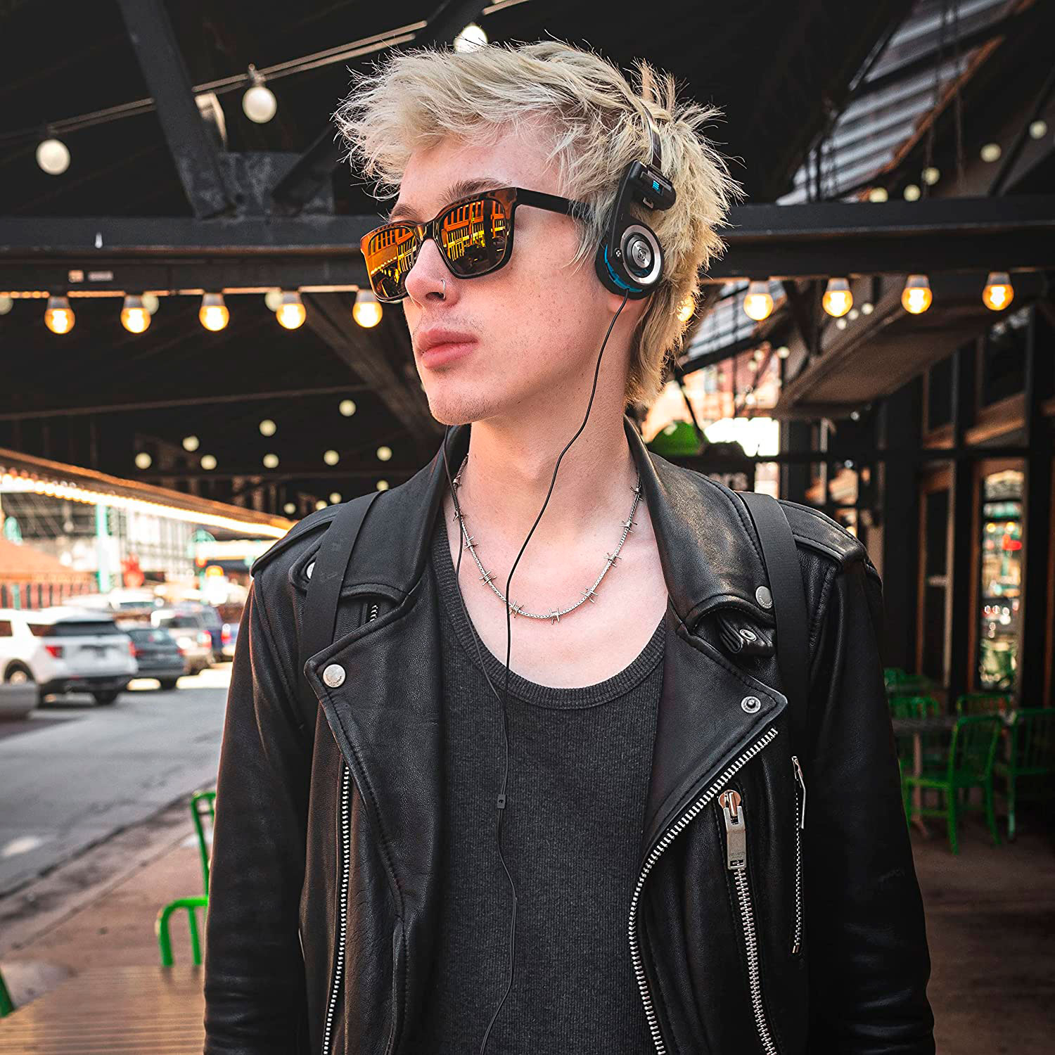 Joven con gafas de sol y auriculares.  Con una chaqueta de cuero negra, de pie en una calle de la ciudad.
