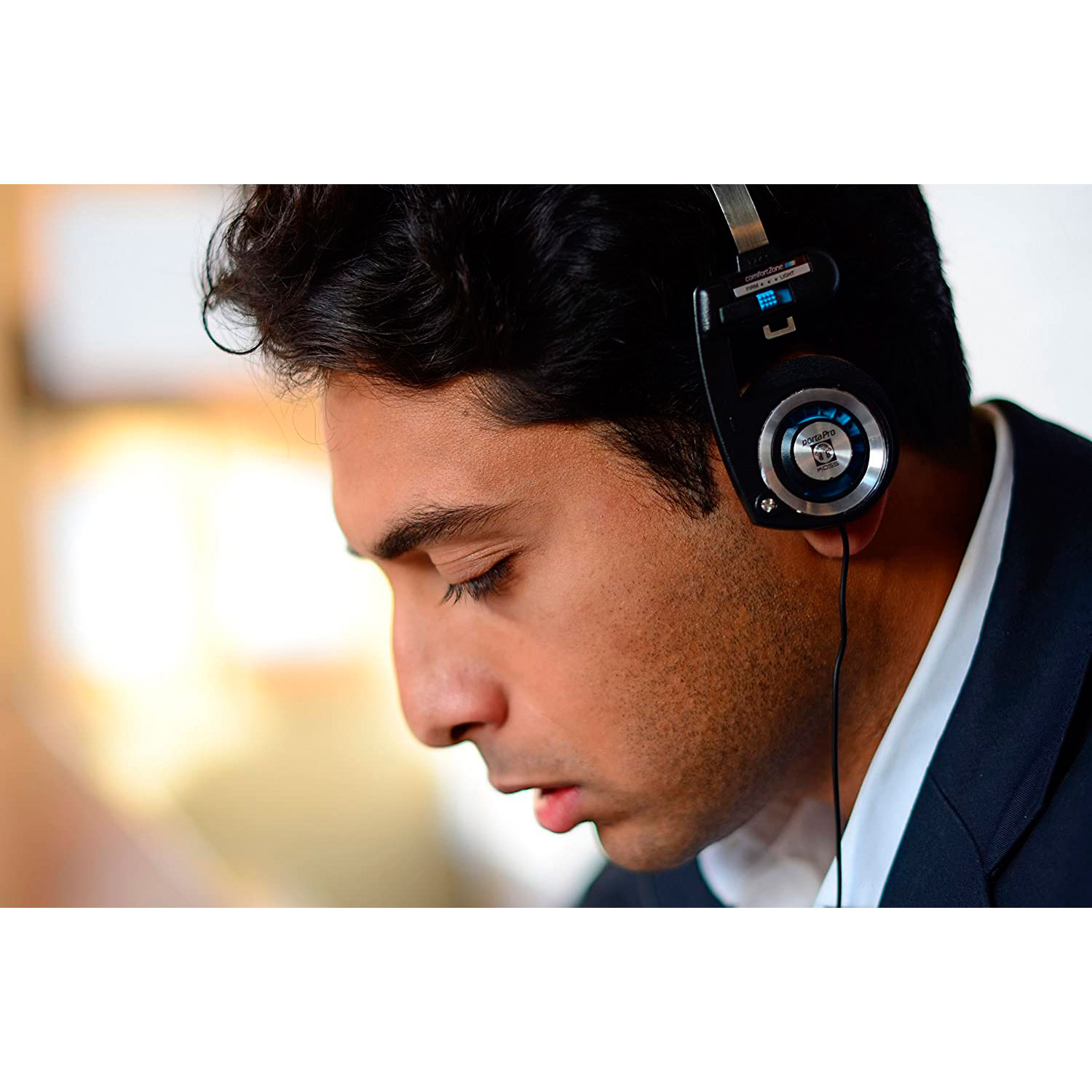 Un hombre con auriculares negros, mirando hacia abajo, en interiores. Fondo borroso.