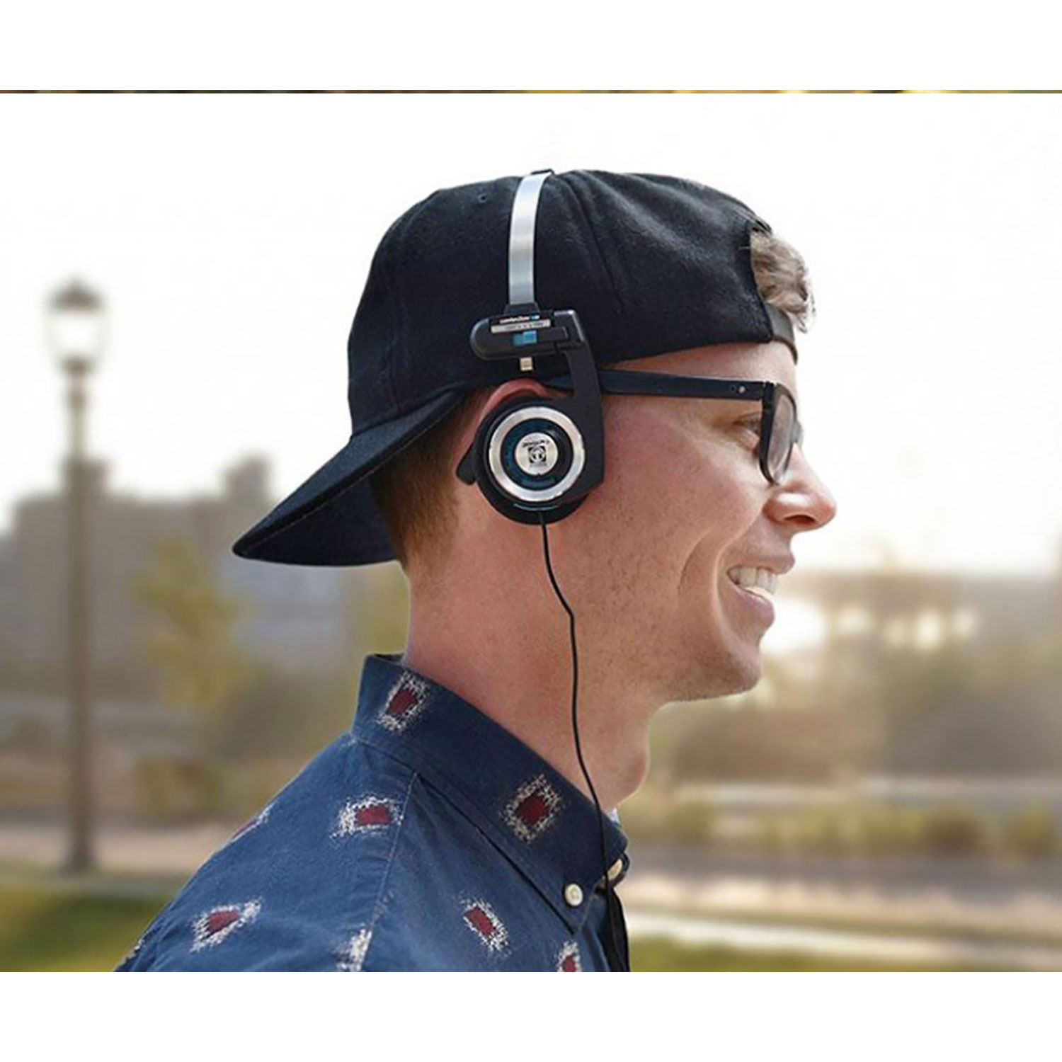 Un hombre con gafas con auriculares, un sombrero negro y una camisa azul sonríe a la cámara.