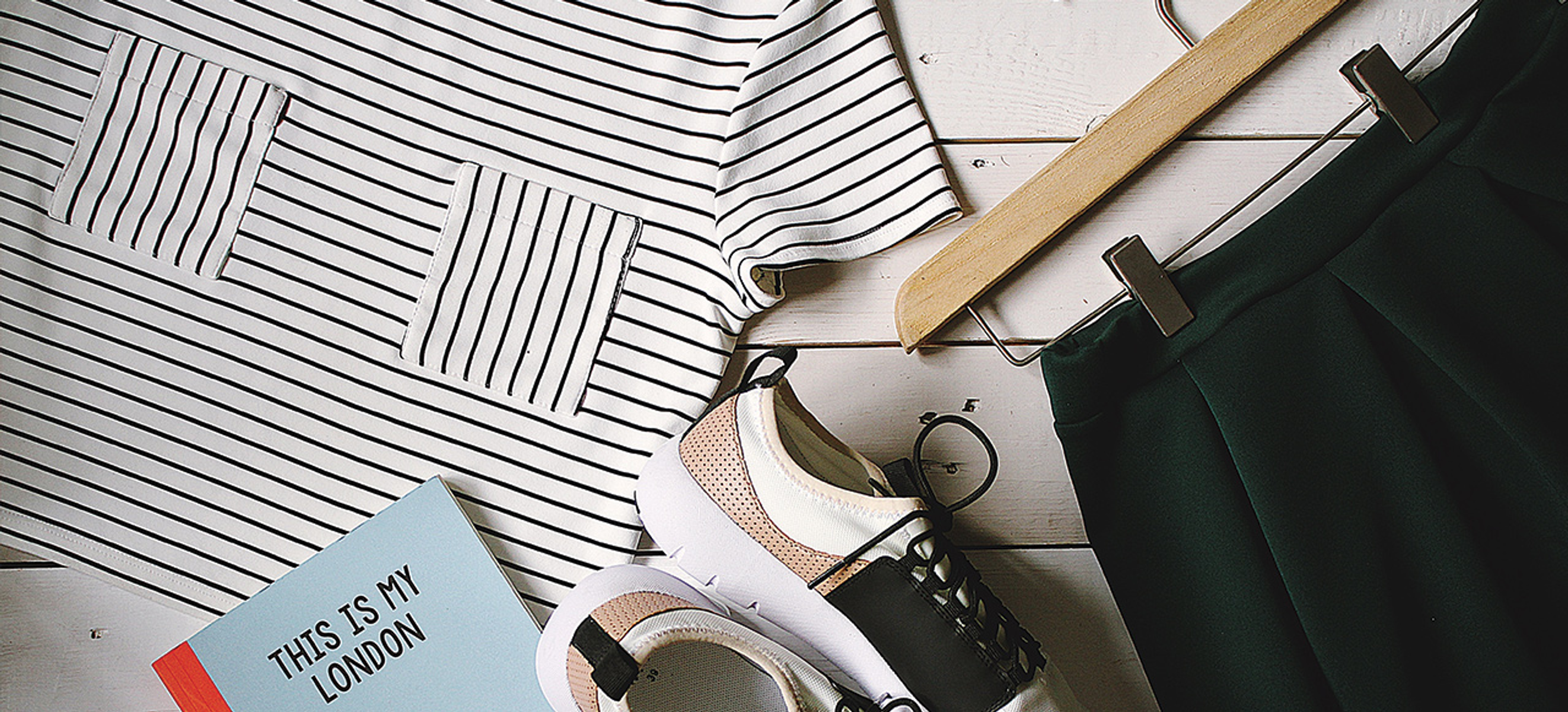 Vista dall'alto di un flat lay di moda. Include camicia a righe, pantaloni scuri, scarpe da ginnastica e un taccuino.