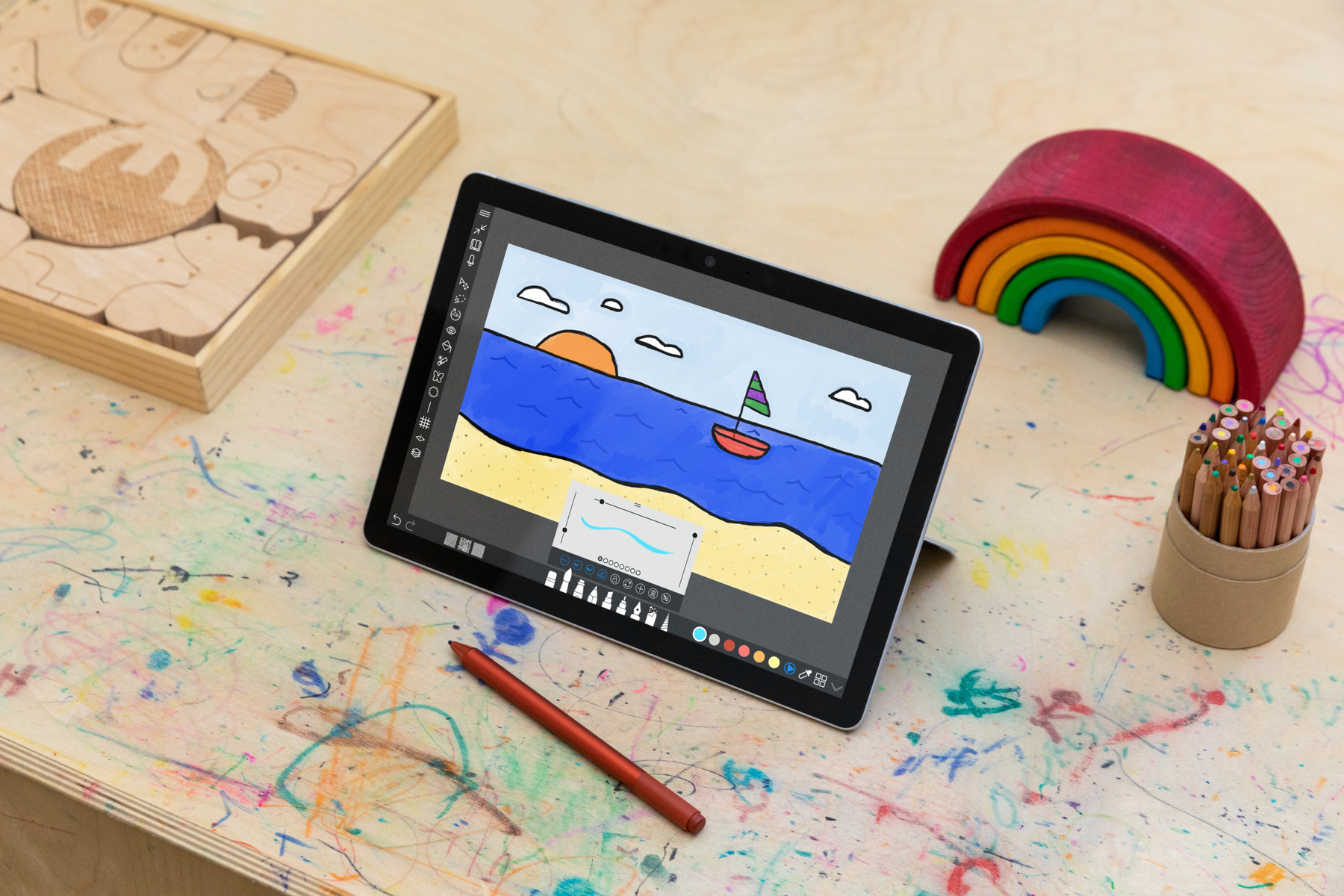 Tablet sul tavolo, disegna una scena sulla spiaggia. Giocattoli in legno, matite, arco.