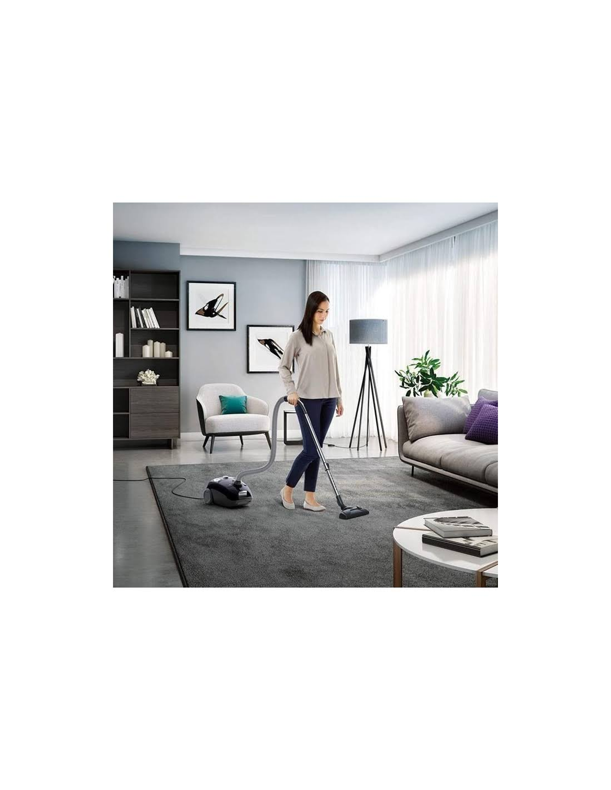 Kobieta odkurza szary dywan. Sofa, obrazy i meble dopełniają scenerię salonu.