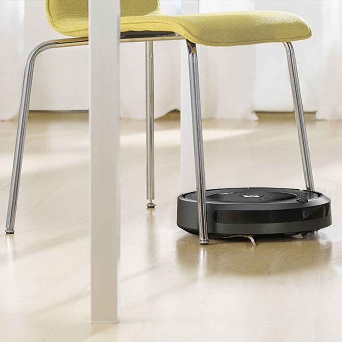 Ein schwarzer Roboter-Staubsauger auf einem Holzboden, unter einem Stuhl.