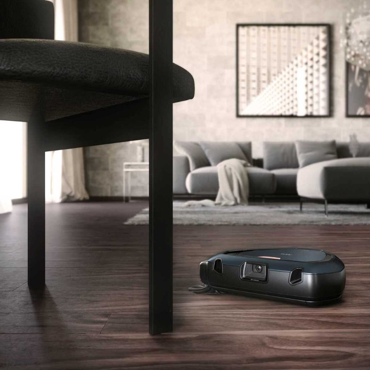 Czarny robot sprzątający pod czarnym stołem, podłoga drewniana.