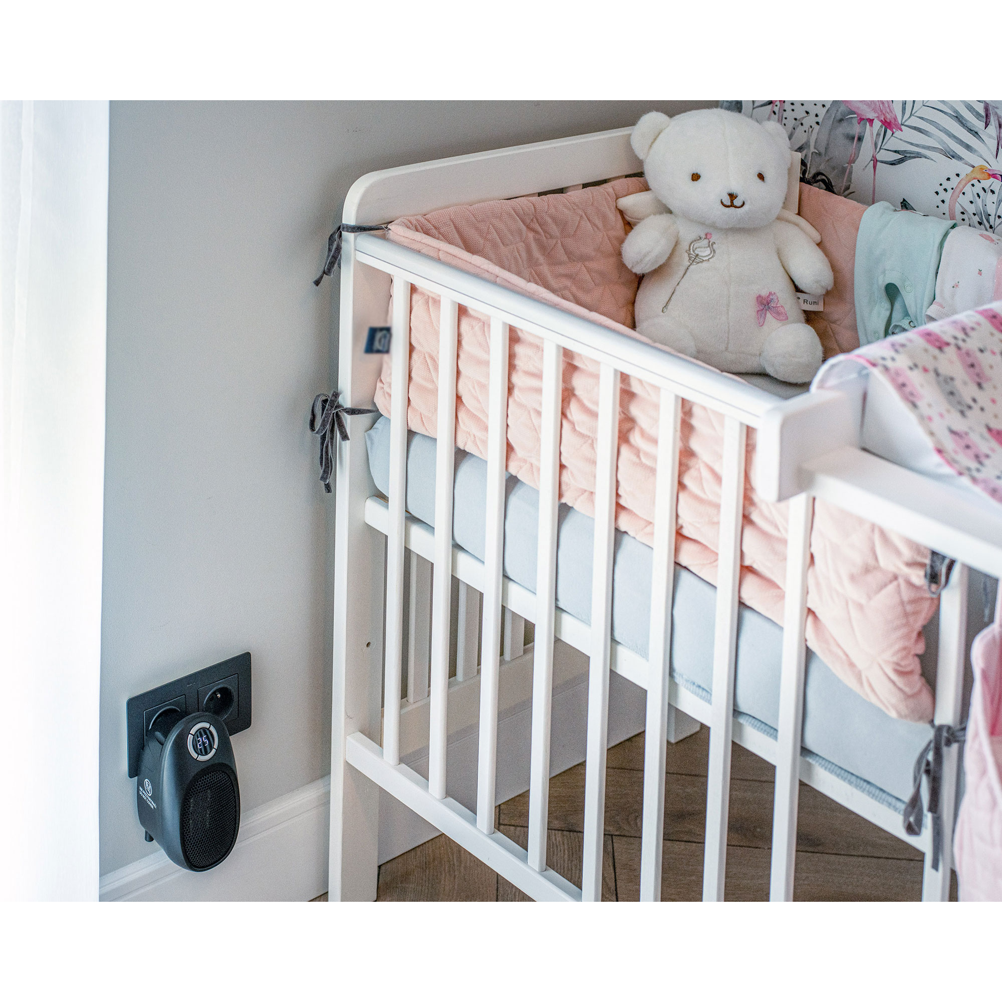 Babybett mit Teddybär, Decken und einem Wandheizkörper daneben.
