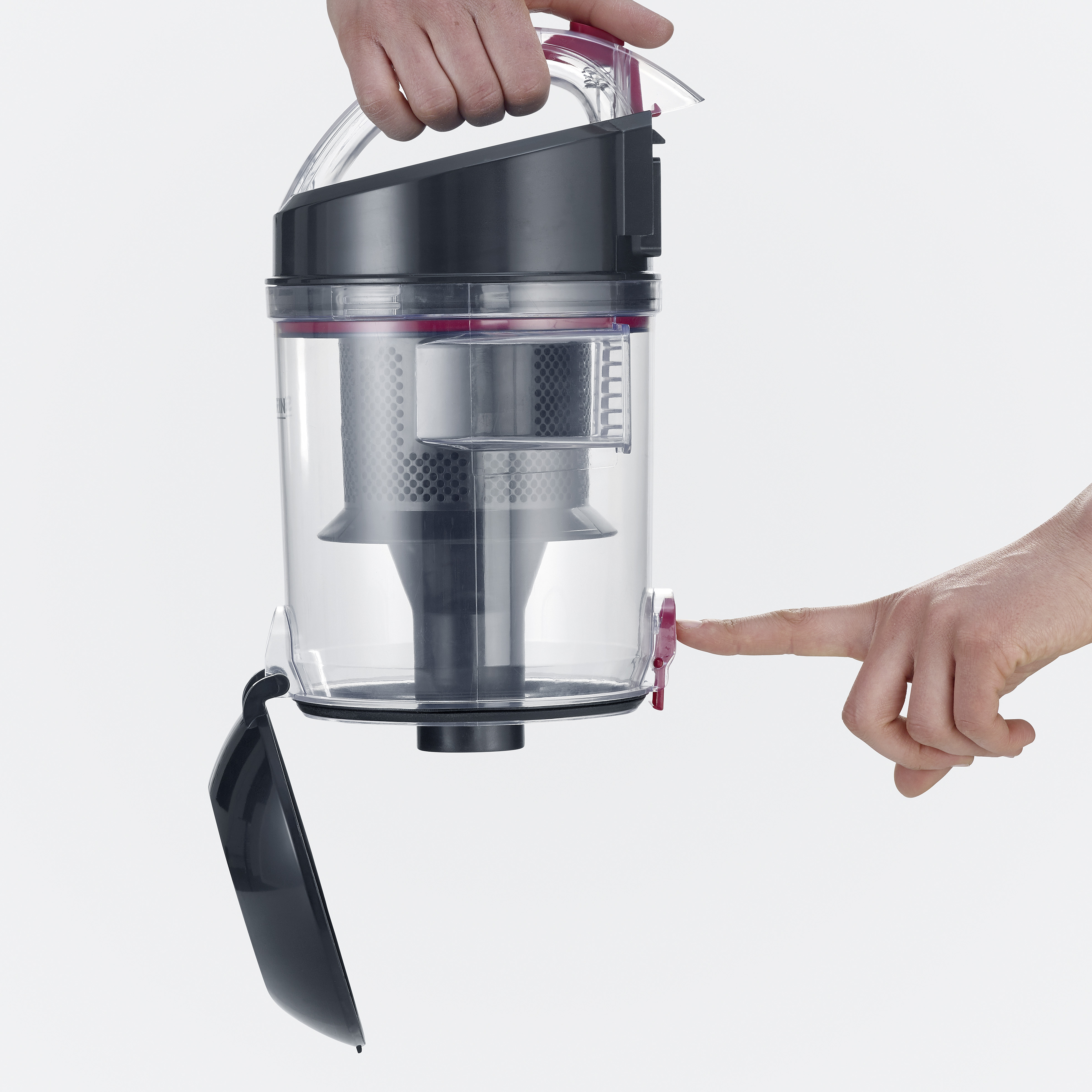 Przezroczysty pojemnik odkurzacza trzymany w dłoniach. Jeden palec naciska czerwony przycisk.