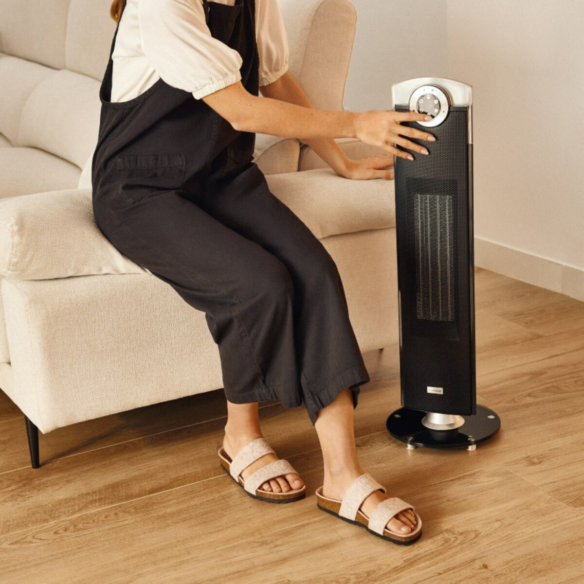 Mujer usando un calefactor negro y plateado sentada en un sofá con sandalias.