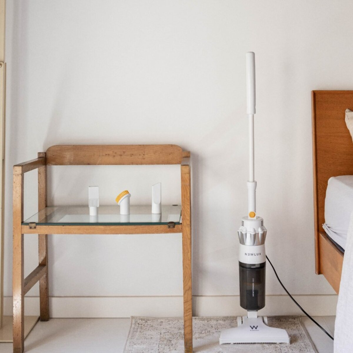 Una aspiradora blanca y una mesa de madera con accesorios de limpieza, contra una pared blanca.