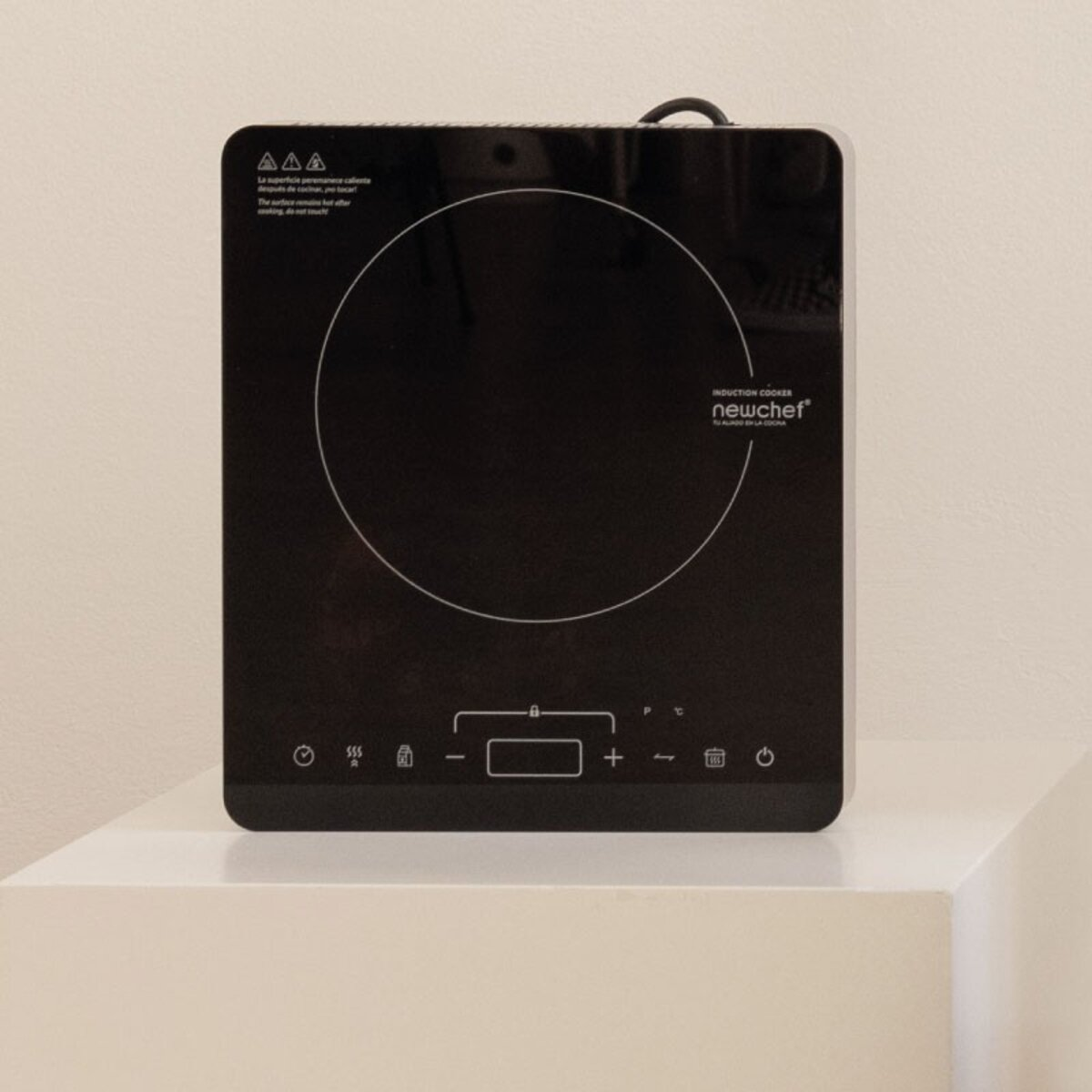 Una cocina de inducción negra sobre una superficie blanca. Tiene controles táctiles.