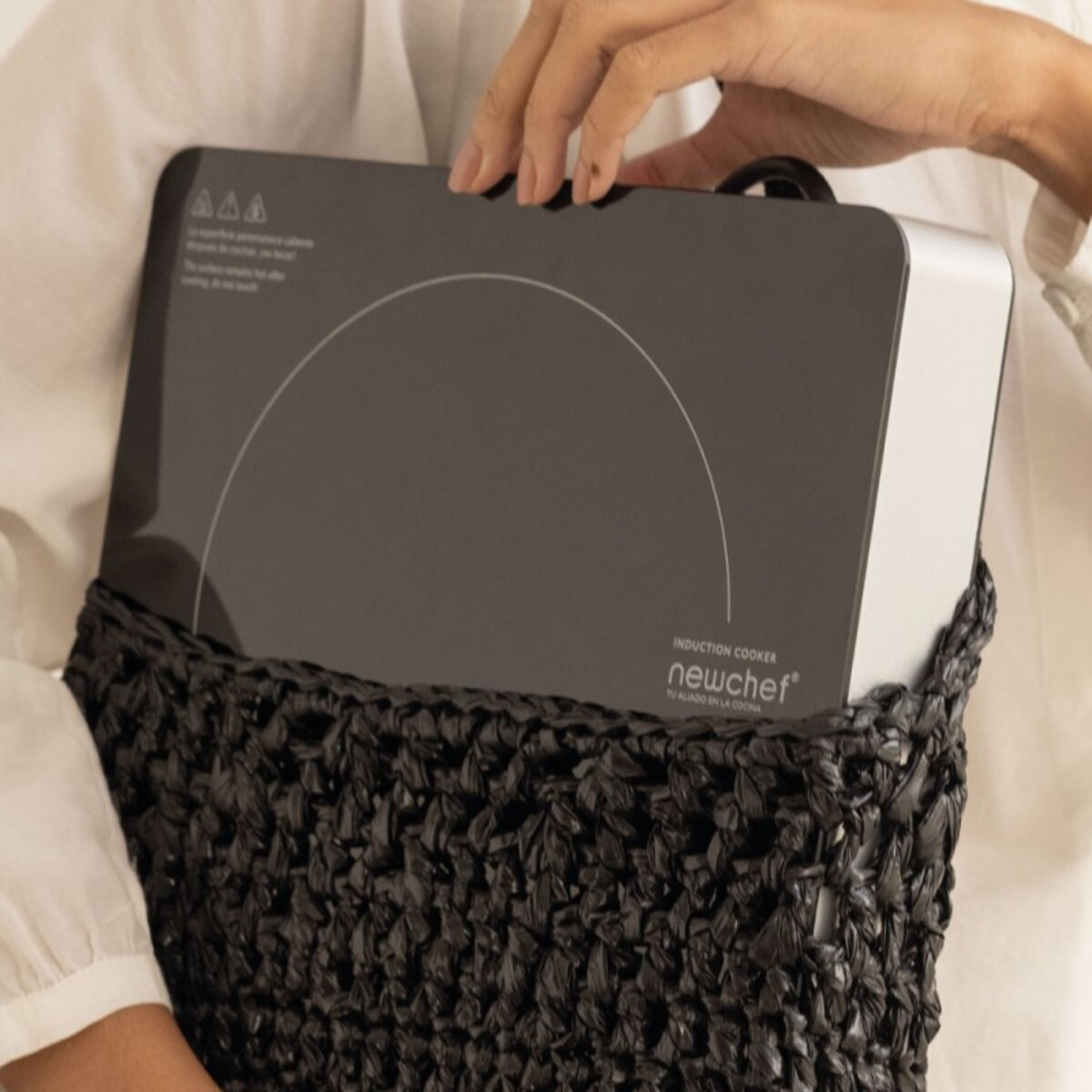 Persona sosteniendo una placa de inducción negra en una bolsa tejida negra. Blanco.