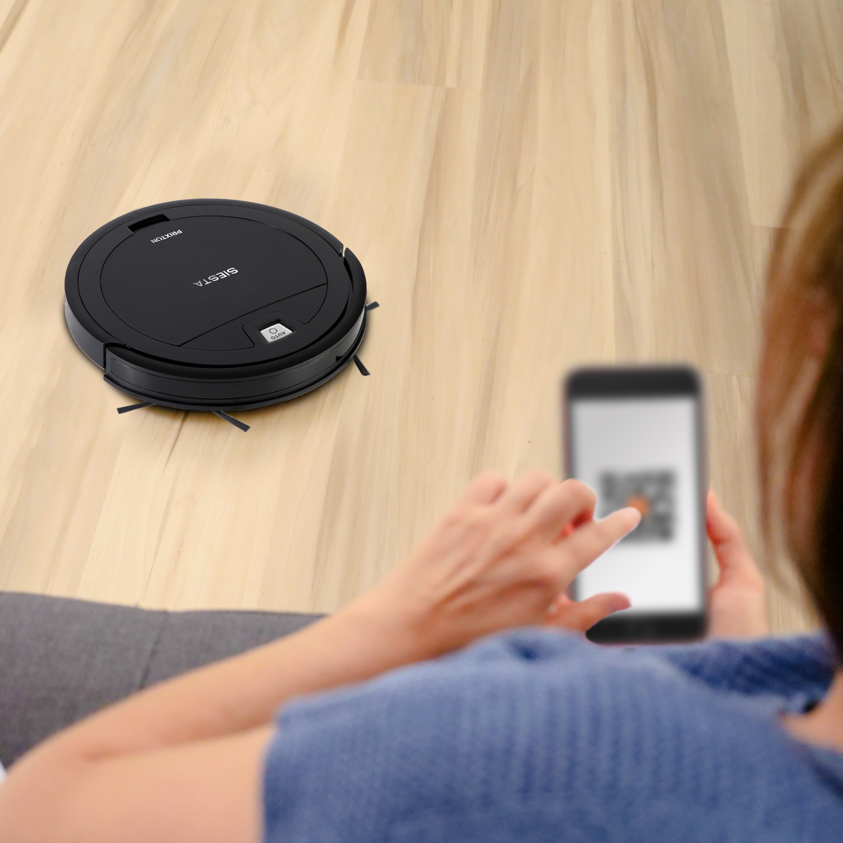 Robot sprzątający na drewnianej podłodze i osoba korzystająca z telefonu z kodem QR.