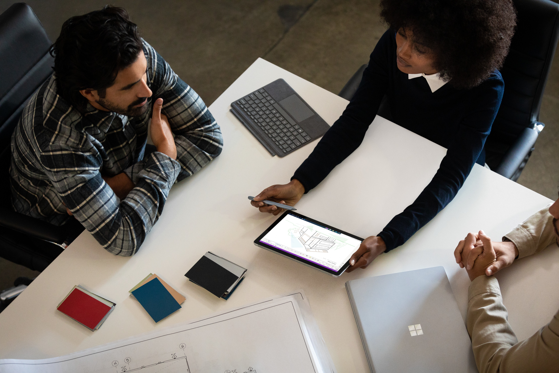 Persone attorno a un tavolo che discutono, con un tablet e una tastiera visibili.