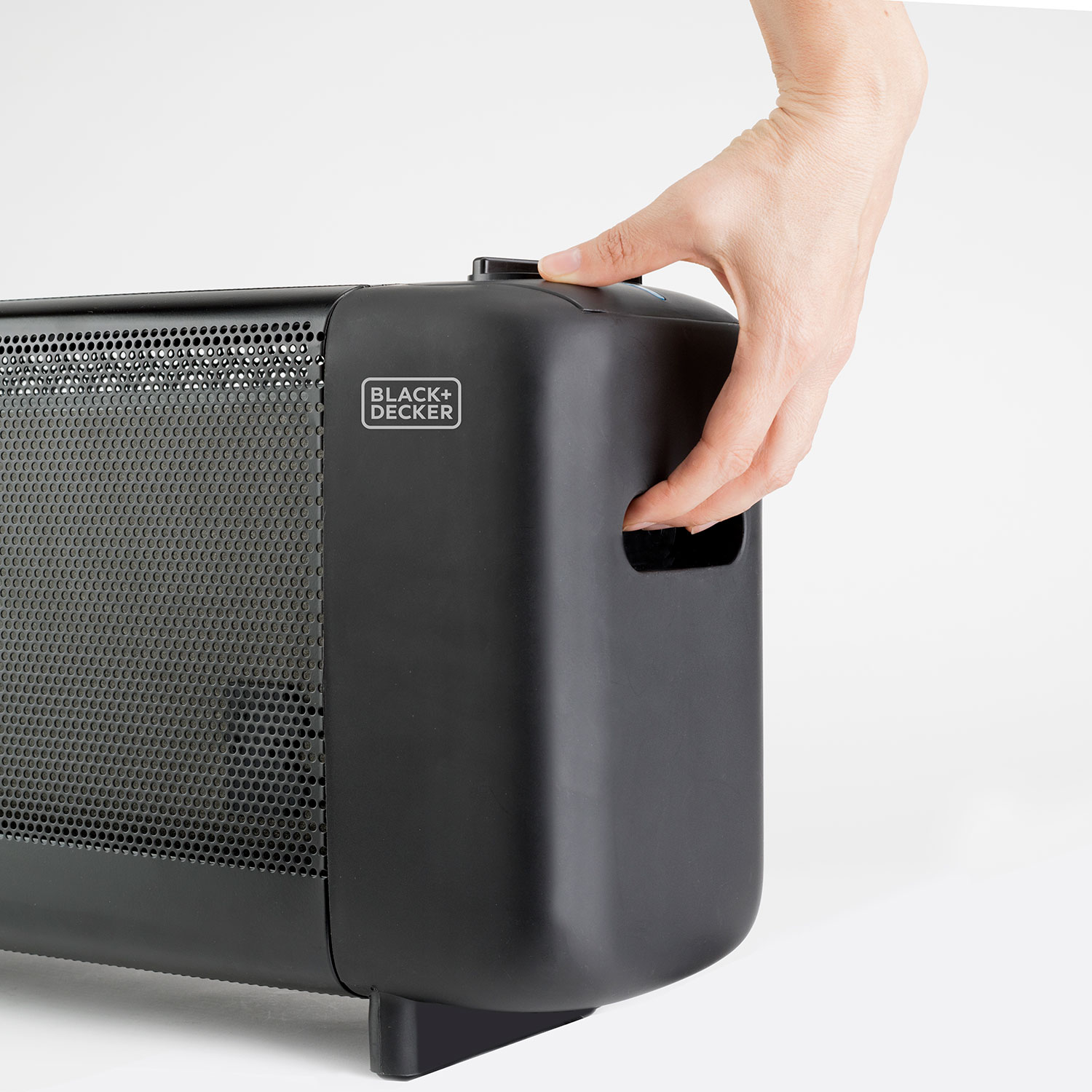Ręka osoby obsługująca czarno-szary grzejnik Black+Decker na białym tle.